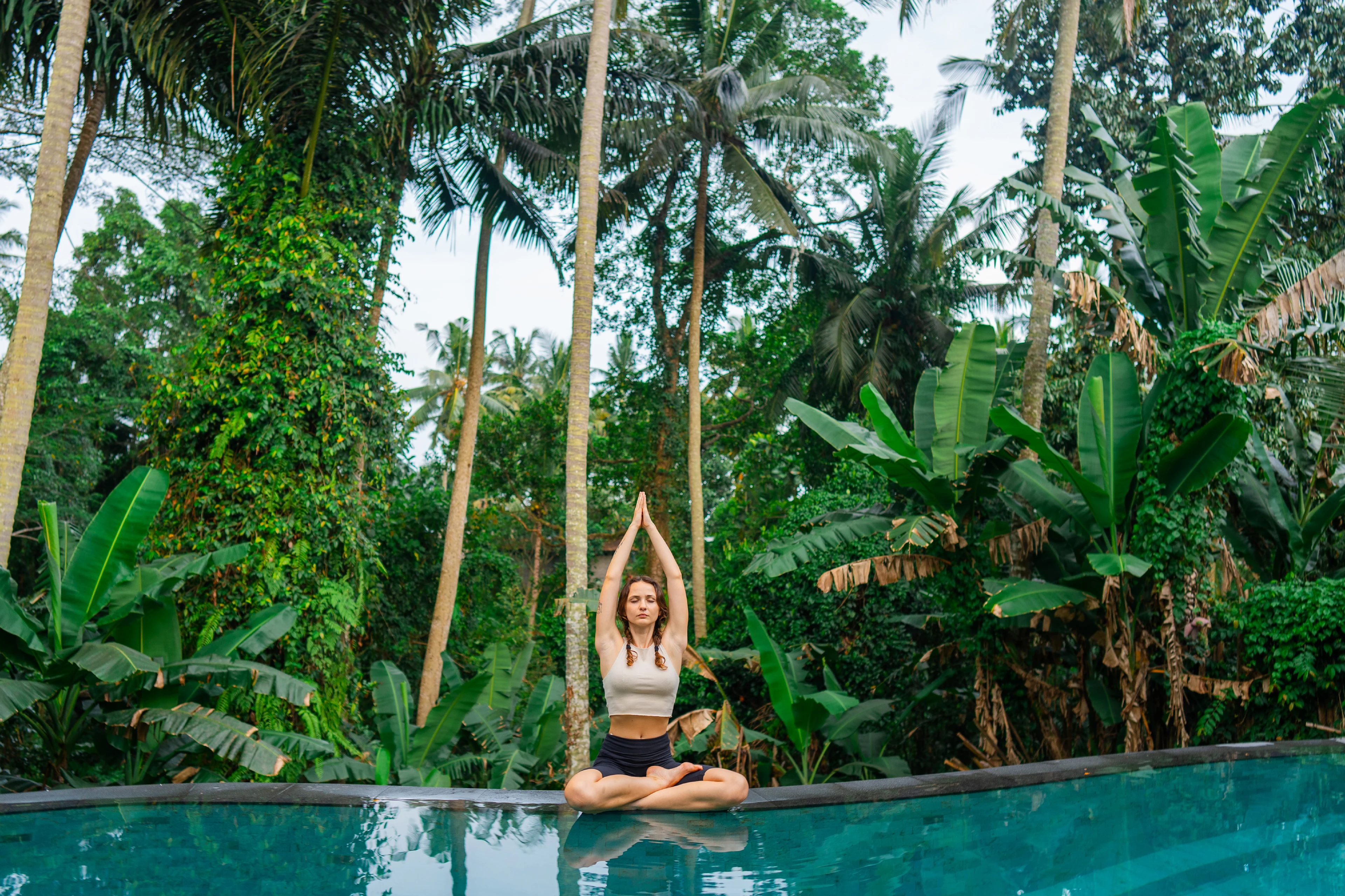 Kvinna som mediterar vid poolkanten i den grönskande djungeln i Ubud på Bali
