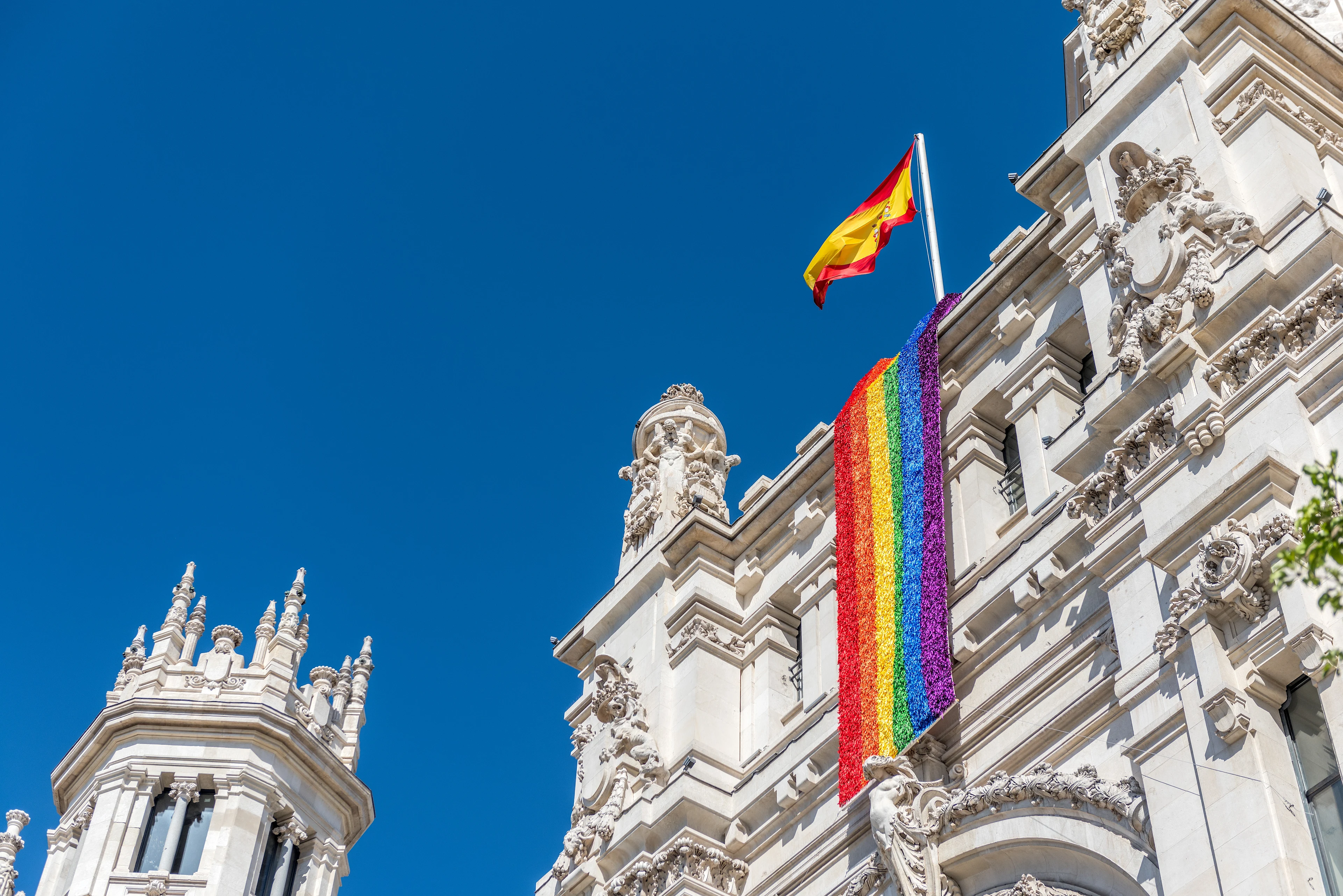 En stor prideflagga längs den vita fasaden på Palacio de Cibeles i Madrid