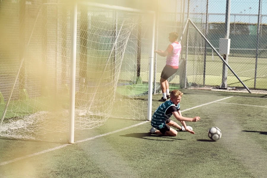 Fotbollsplan med en pojke i mål som försöker fånga en fotboll