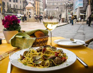 Lautanen spaghettia alle vongolea ja lasillinen valkoviiniä tarjoillaan ulkoterassilla aukiolla Italiassa