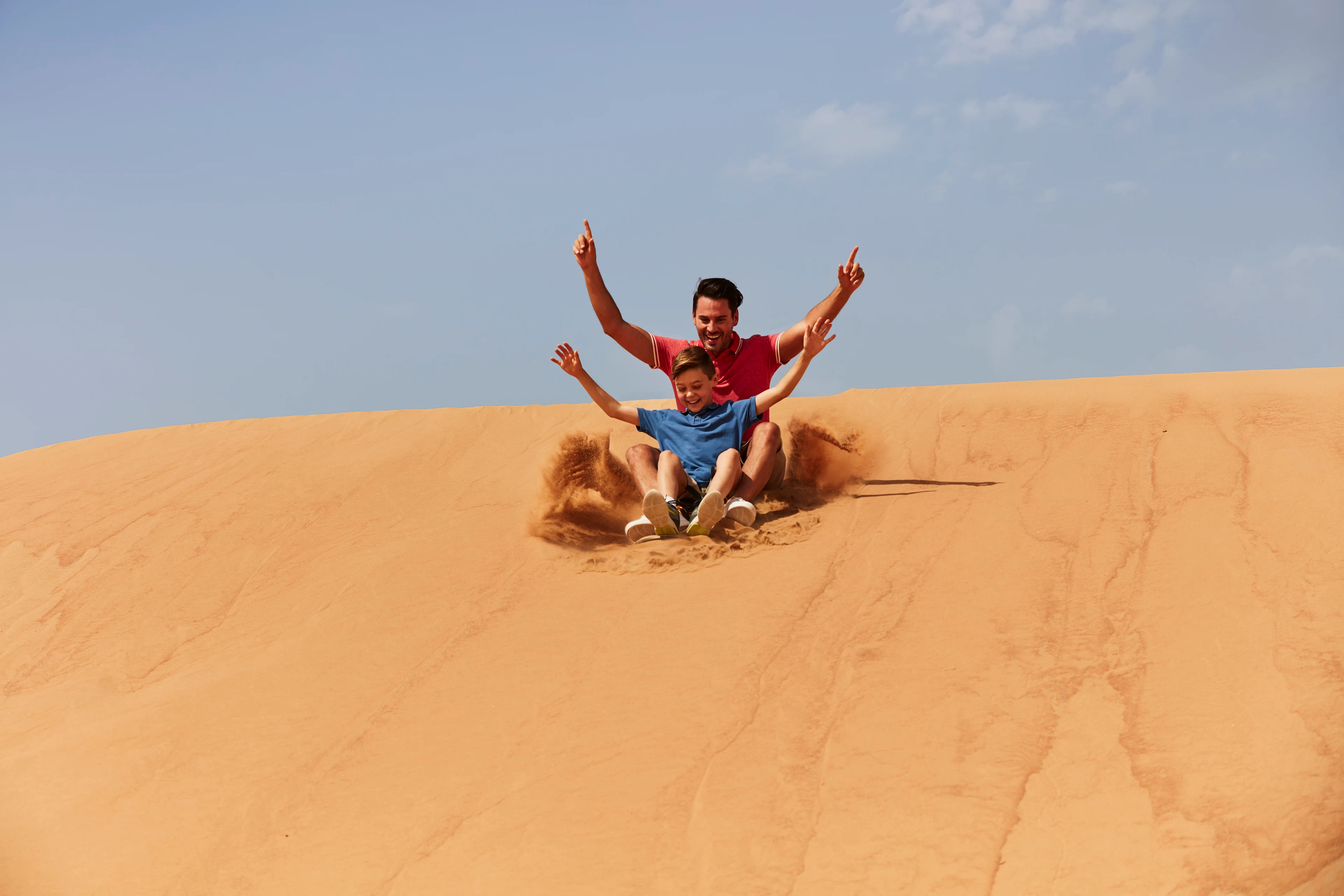 Pappa och son åker sandboarding i öknen