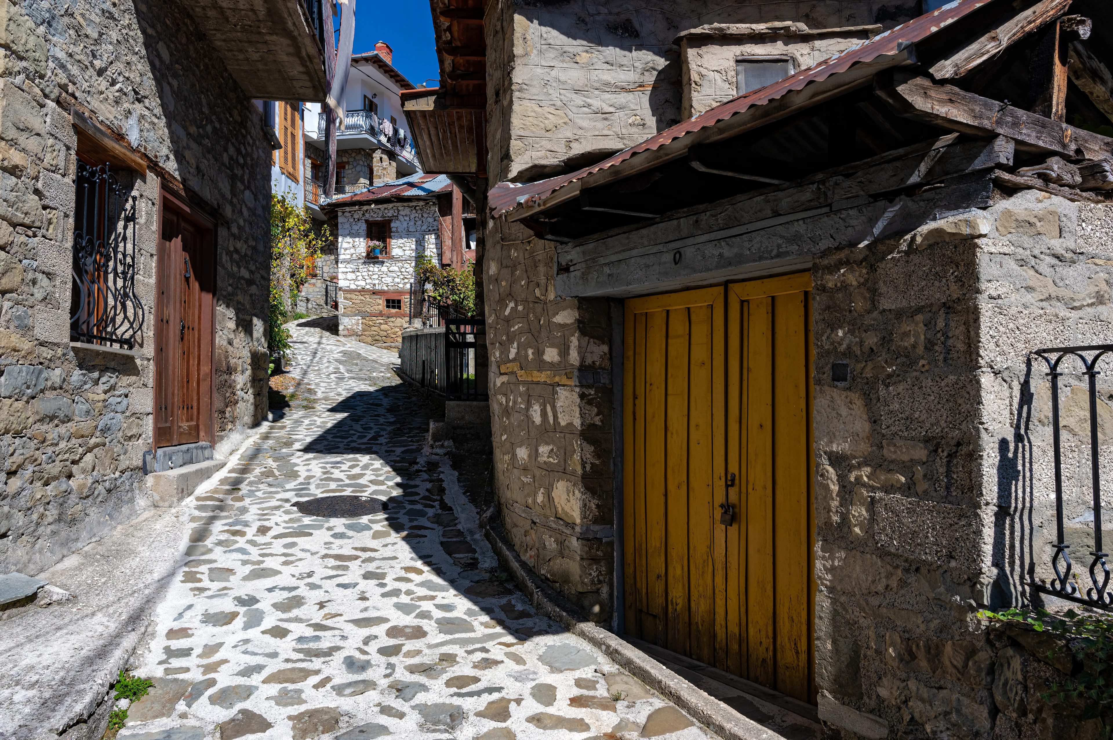 Kullerstensgränd med traditionella stenhus och träbalkonger i bergsbyn Metsovo i Epirus.