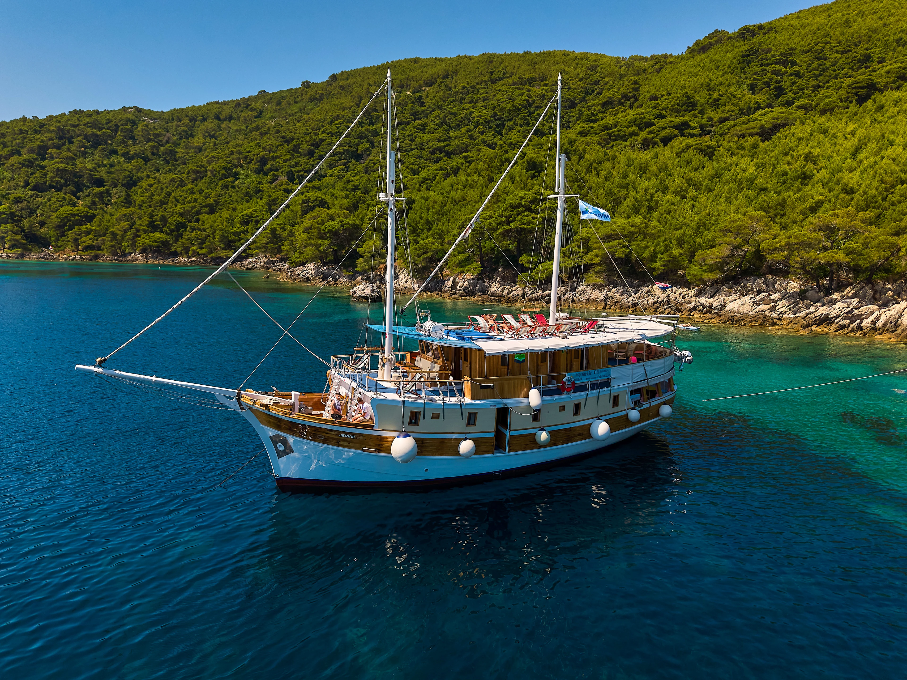 Suuri purjevene on ankkuroituna kirkkaan siniseen mereen lähellä rehevää vihreää rannikkoa