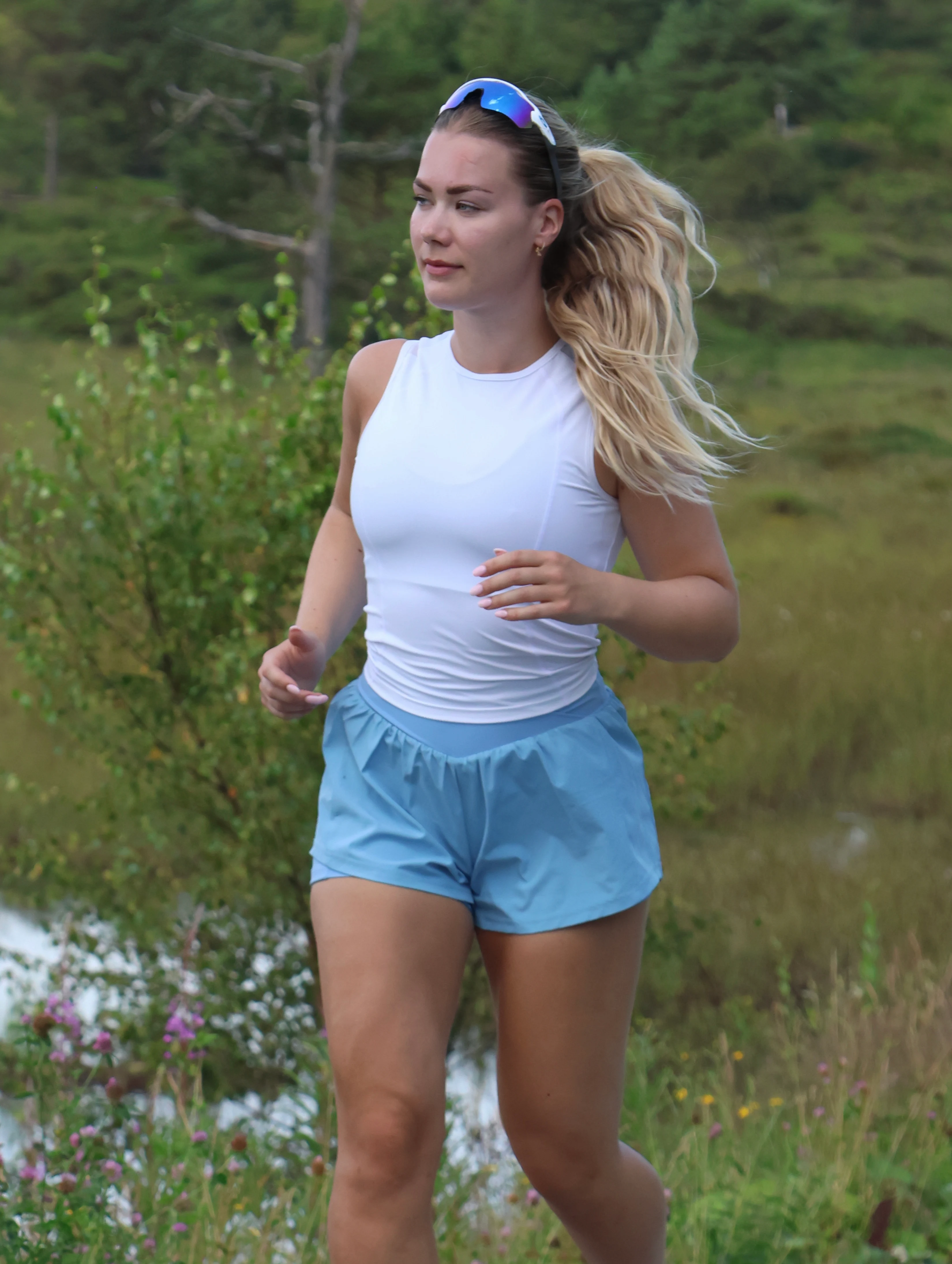 Kjersti Halland Sudmann løper i skogen ikledd hvit singlet og lys blå løpeshorts