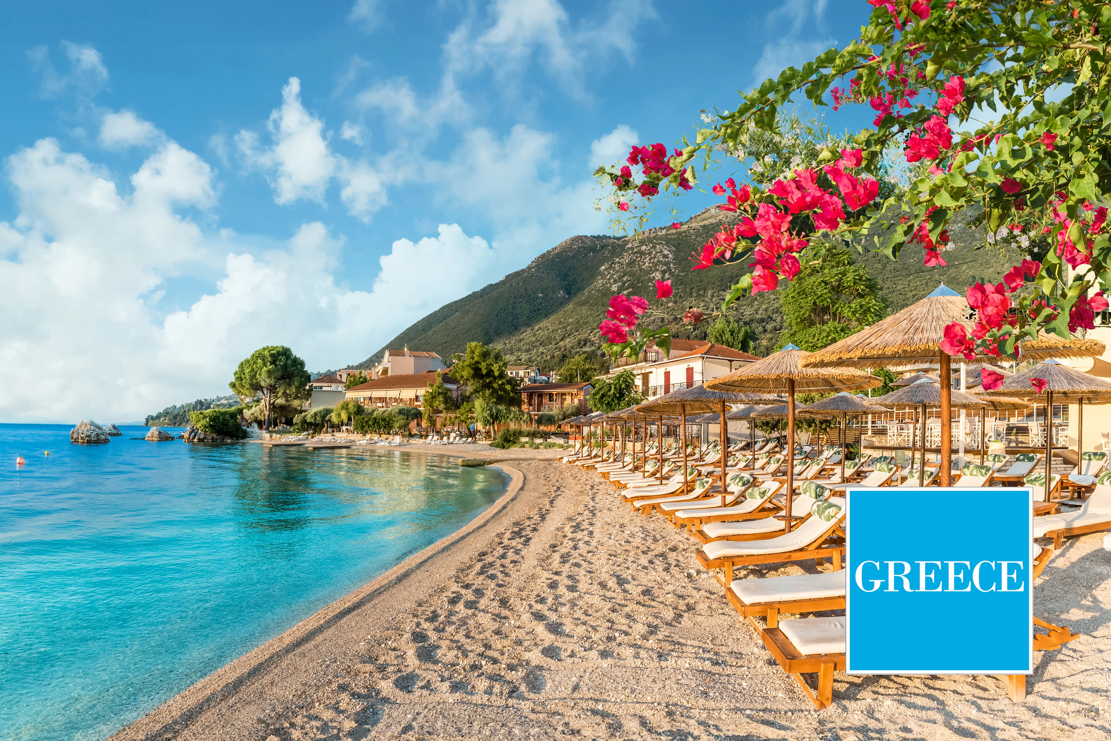 Soliga solstolar på en vacker strand i Grekland med klart blått hav, blommande bougainvillea och gröna berg i bakgrunden.