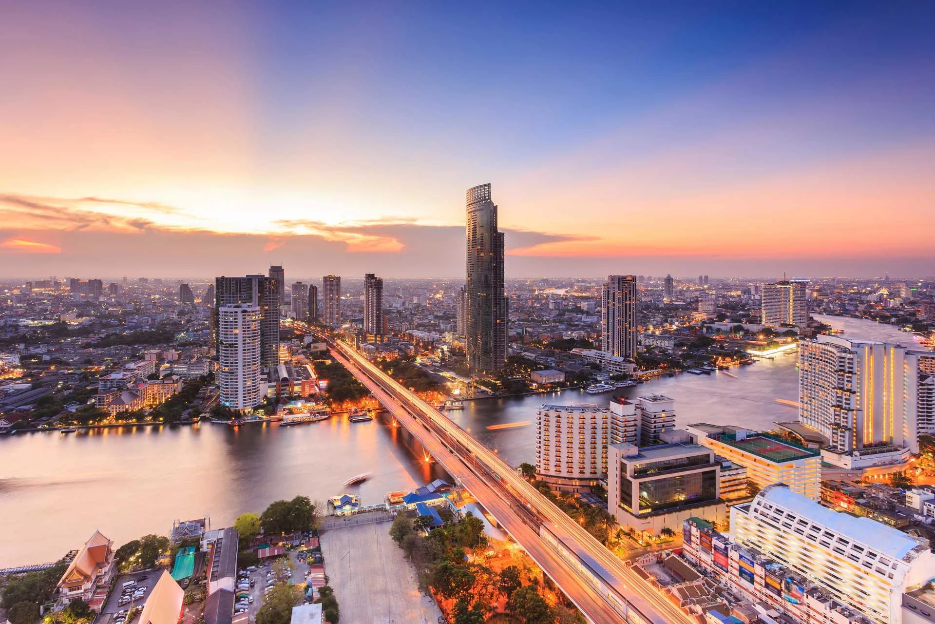Panoramavy över Bangkok i skymningen med skyskrapor, Chao Phraya-floden och en upplyst bro som sträcker sig genom stadens livliga centrum.