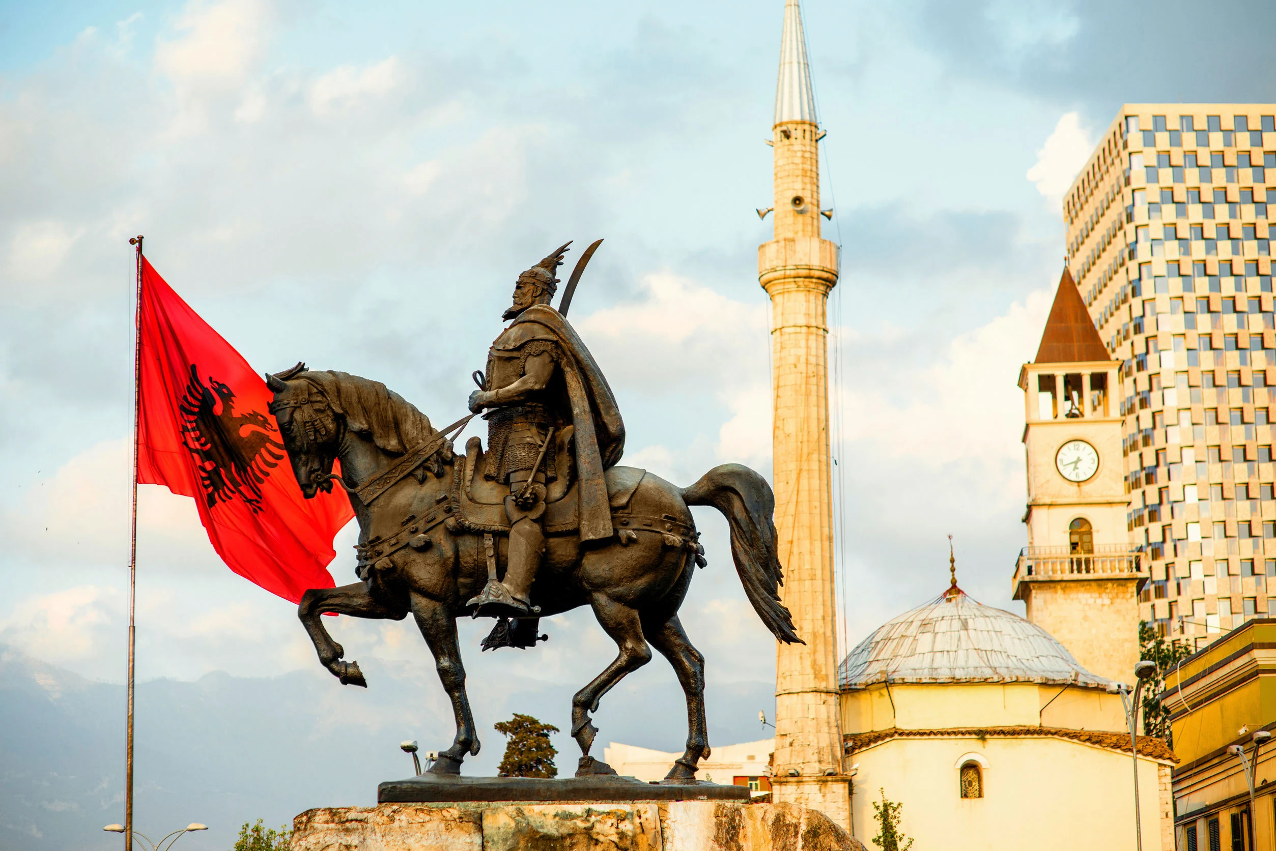 Een standbeeld van een man op een paard met de vlag van Albanië op de achtergrond