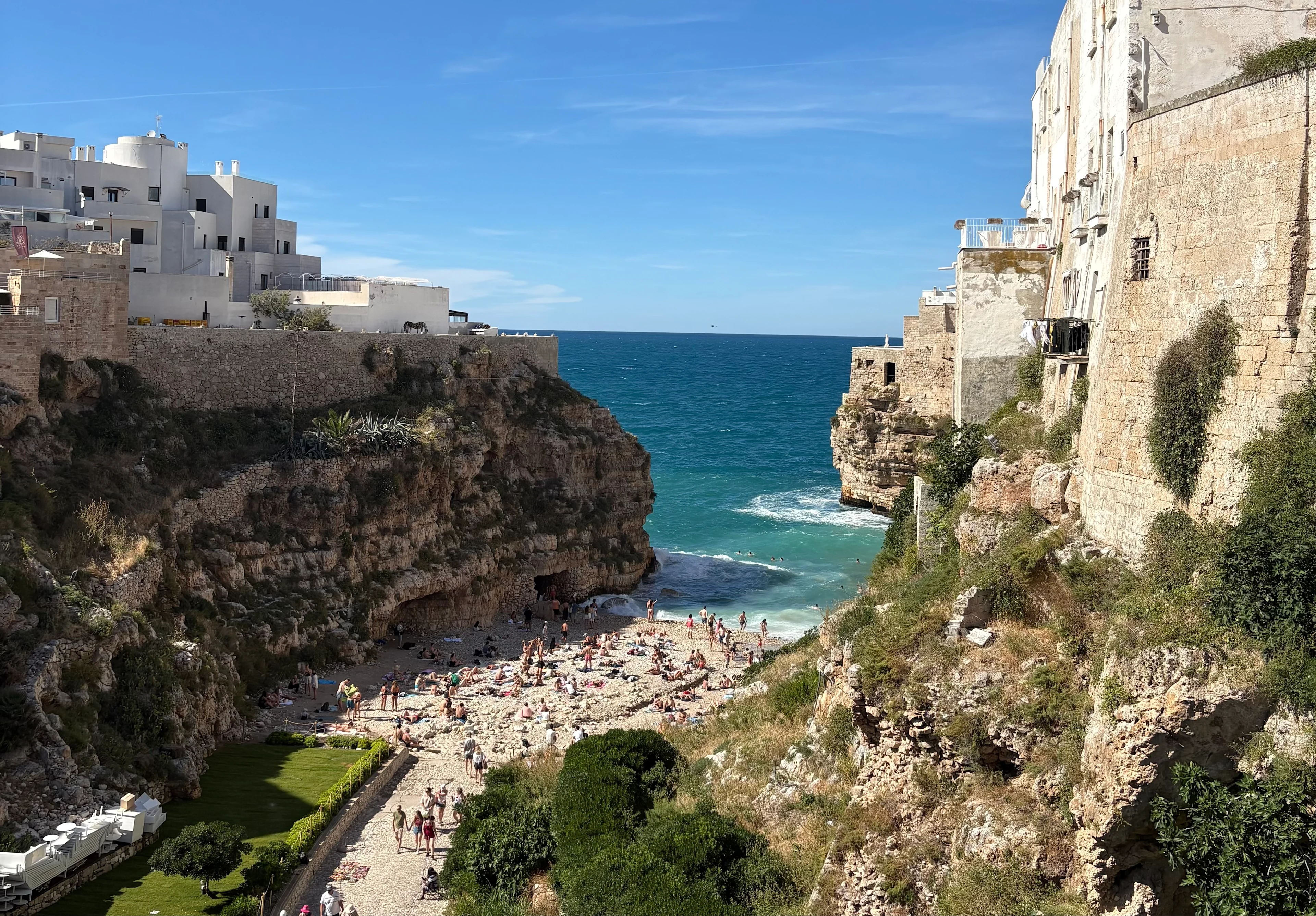 Strand mellan höga klippor och historiska byggnader vid det turkosblå havet i Polignano a Mare.