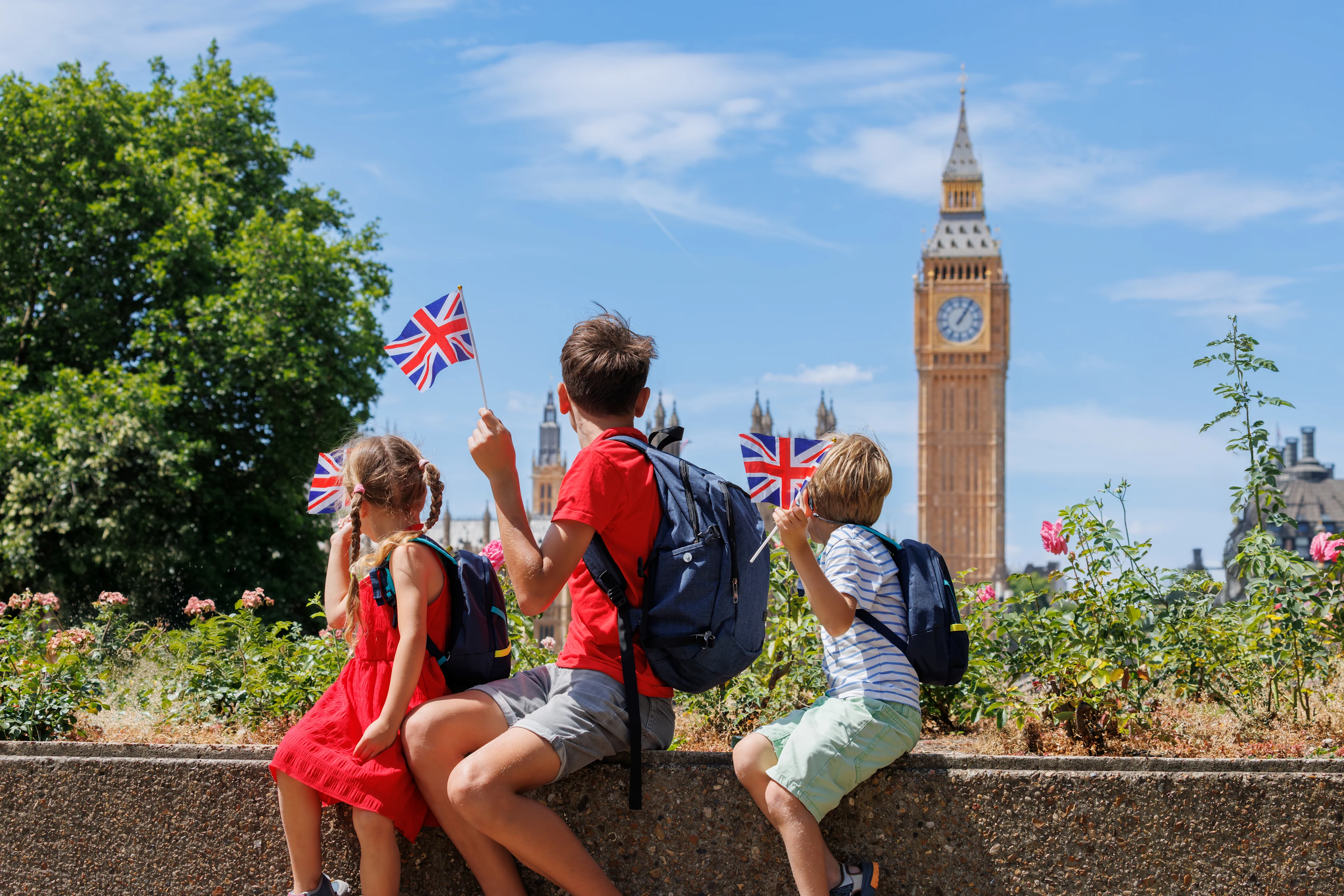 Barn med små britiske flagg sitter i en park i London med Big Ben og Westminster i bakgrunnen.