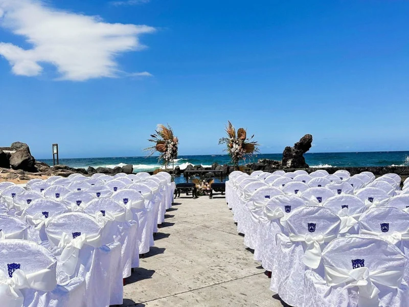 Bilde av plasser for bryllupsgjester i hvitkledde stoler med blå himmel og blått hav i bakgrunnen . der man kan gifte seg