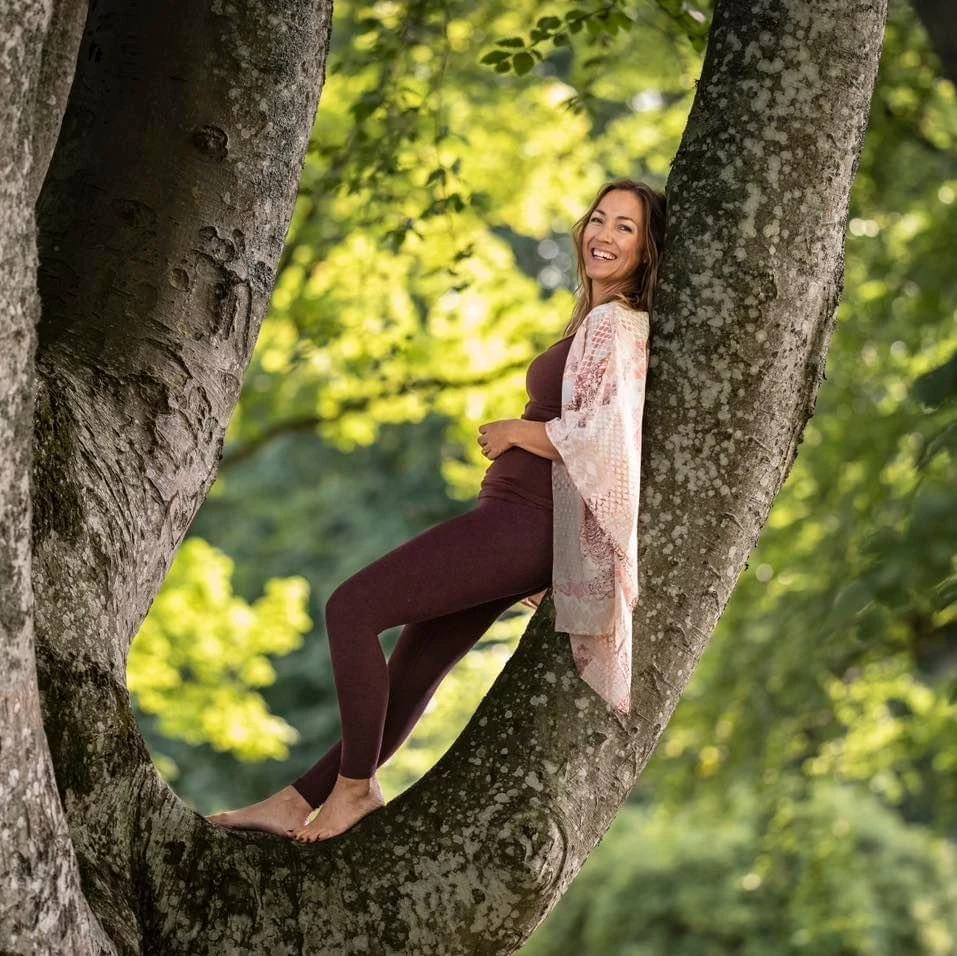 Cecilie H. Eggen som står i et tre med brune treningtights og topp med en florlett åpen bluse over. 
