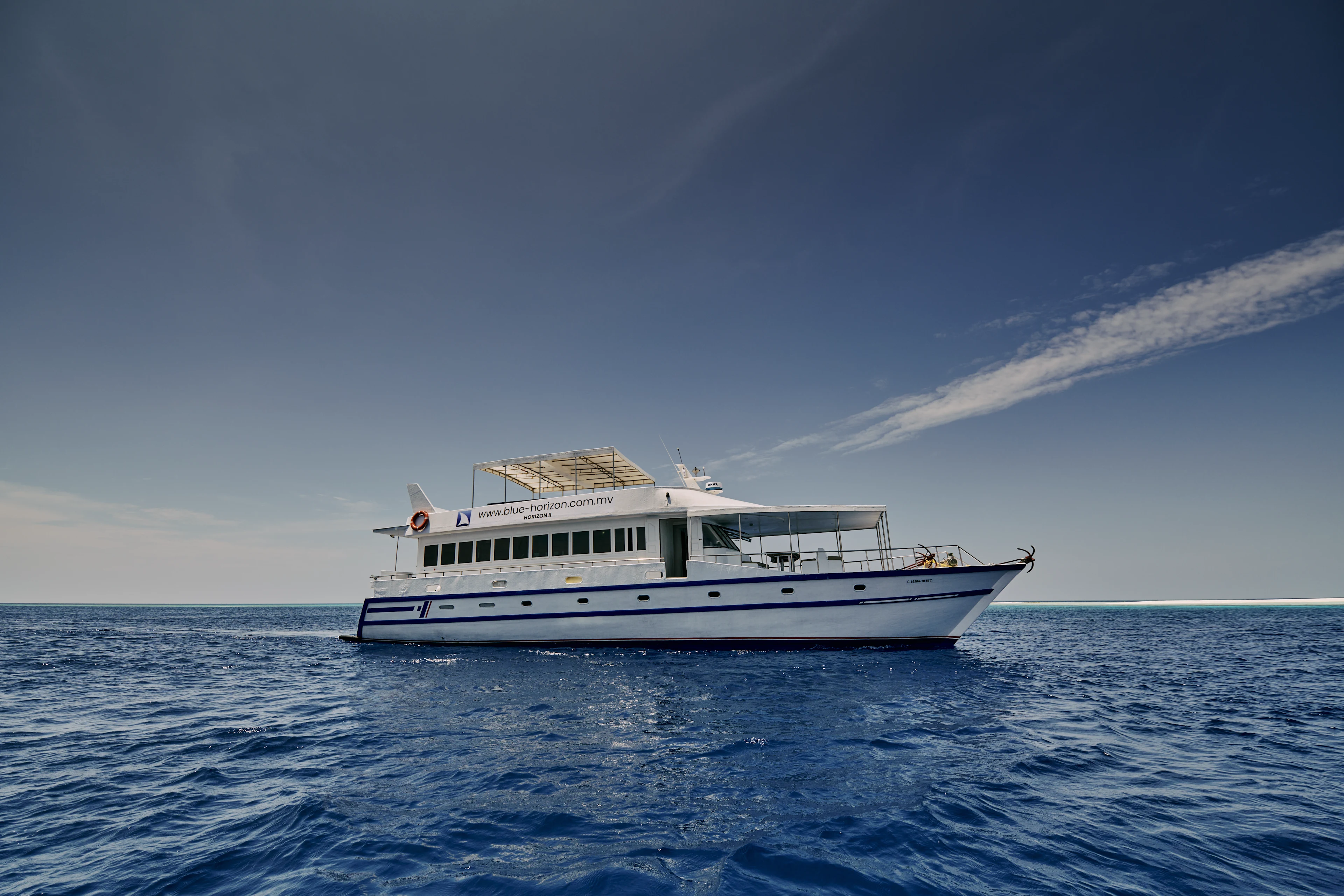 En större vit båt ligger stilla på öppet hav under en klar himmel