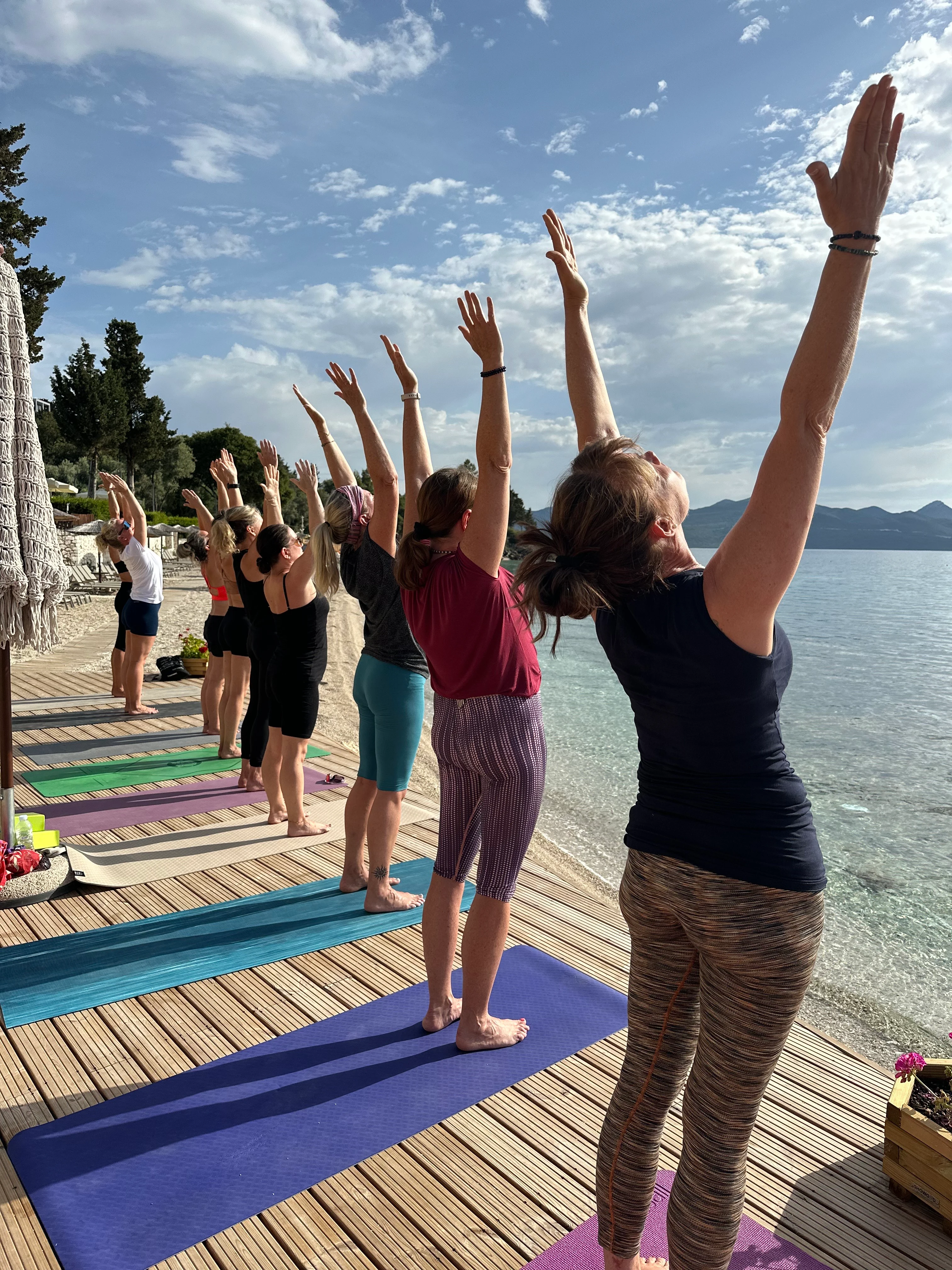 En gjeng med damer som gjør solhilsen på en treplattform ved stranden.