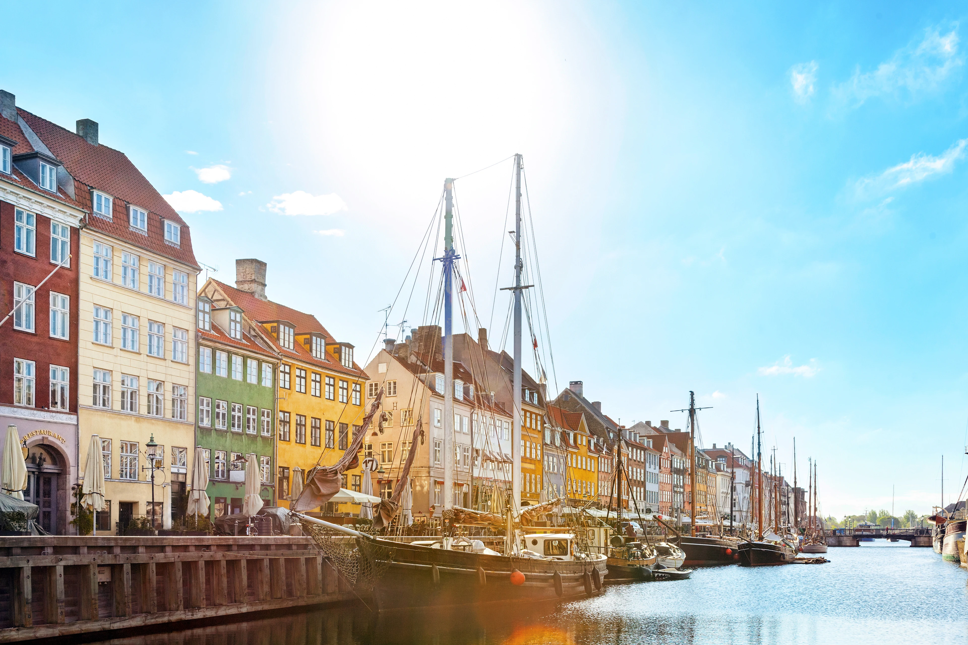 Färgglada husfasader och segelbåtar längs Nyhavn i Köpenhamn en solig dag, med lugnt vatten.