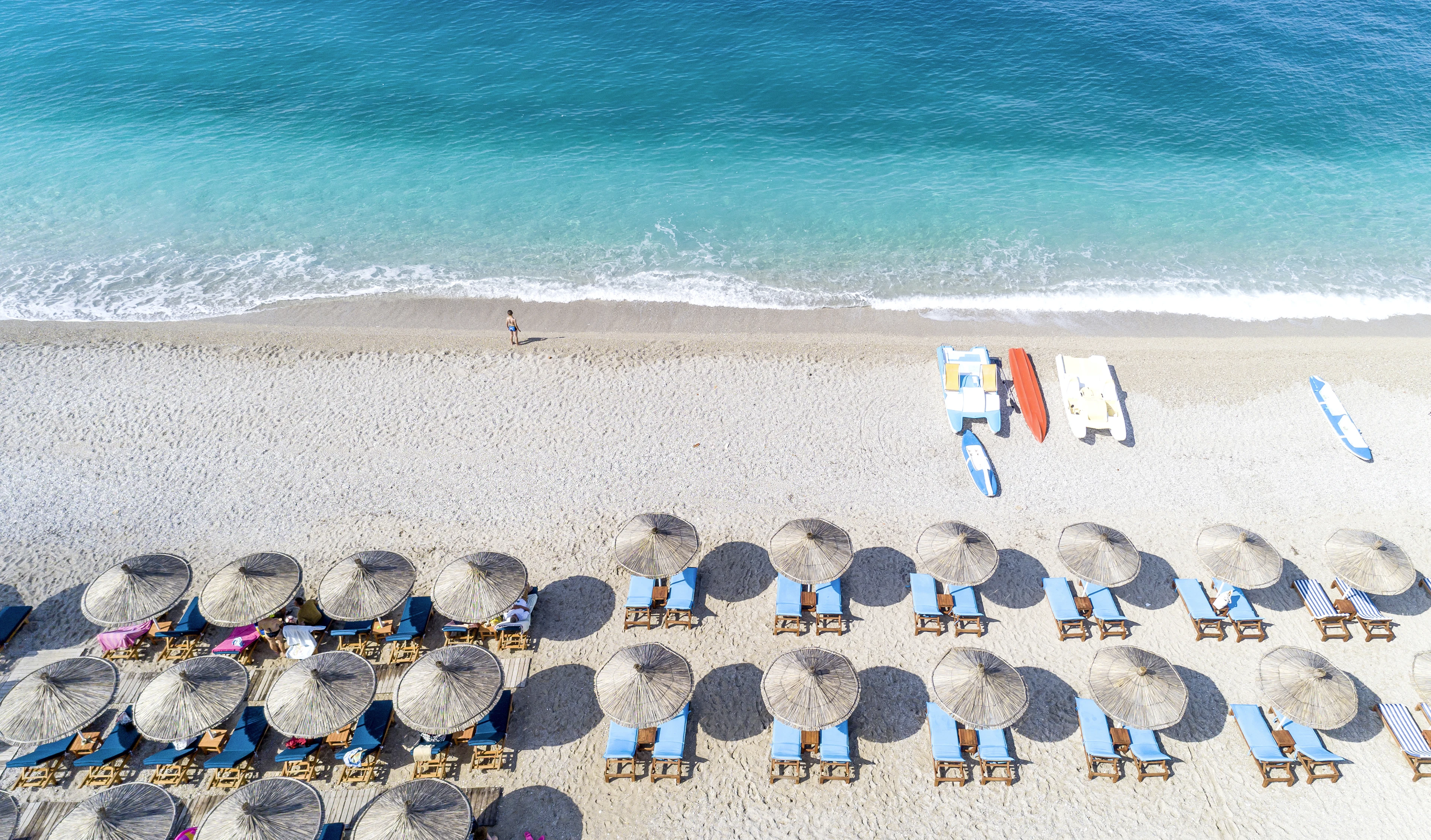 Sandstrand i Dhermi med turkostvatten och solstolar och parasoll längs stranden