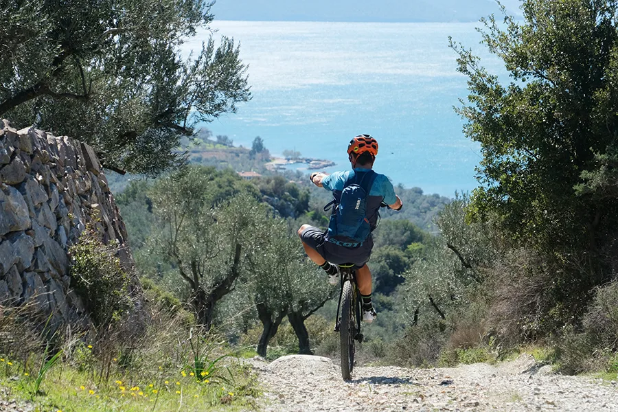 Cyklist åker på bakhjulet av cykeln på ett berg med utsikt över havet