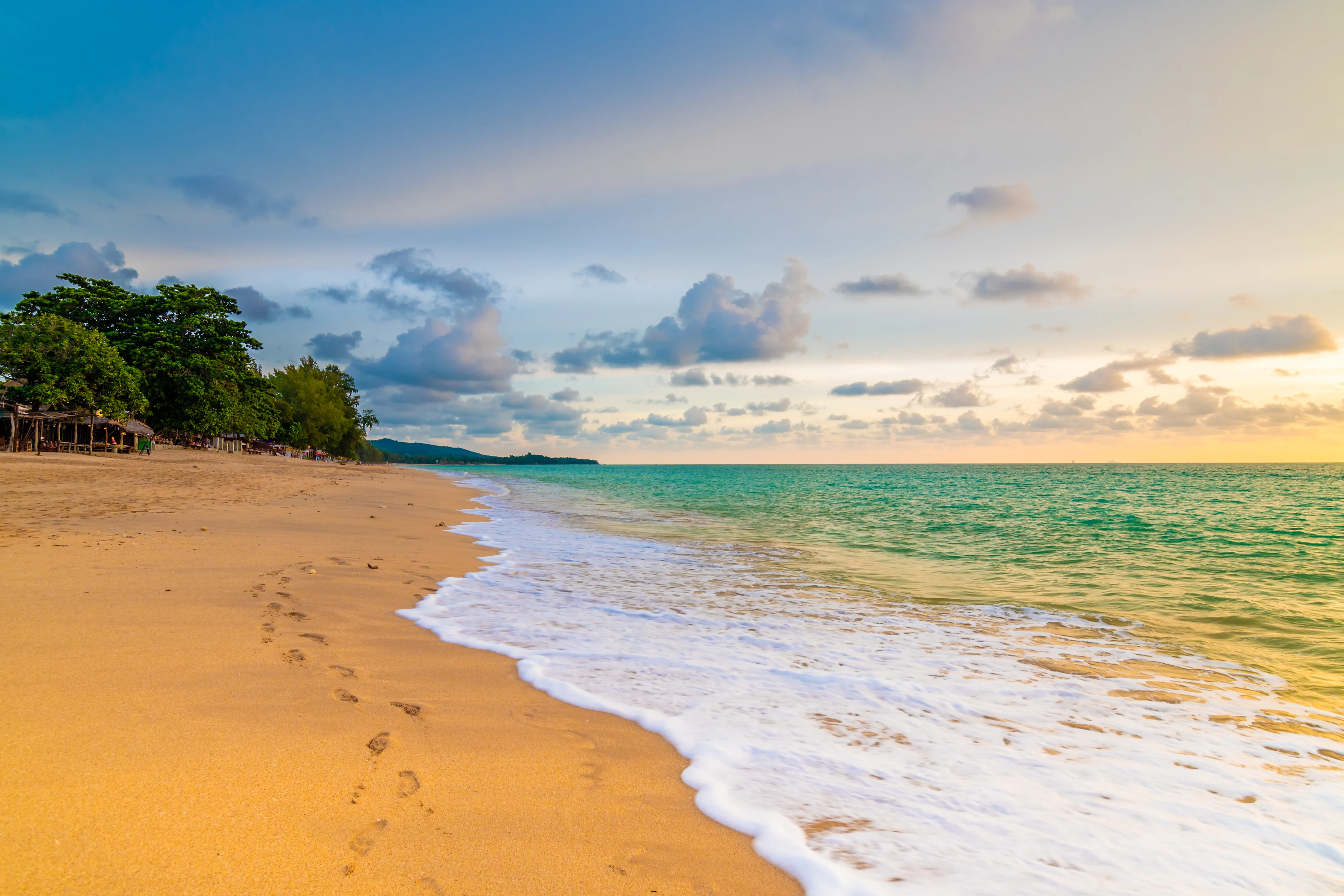 Lång sandstrand på Koh Lanta med turkost hav, mjuka vågor och fotspår i sanden.