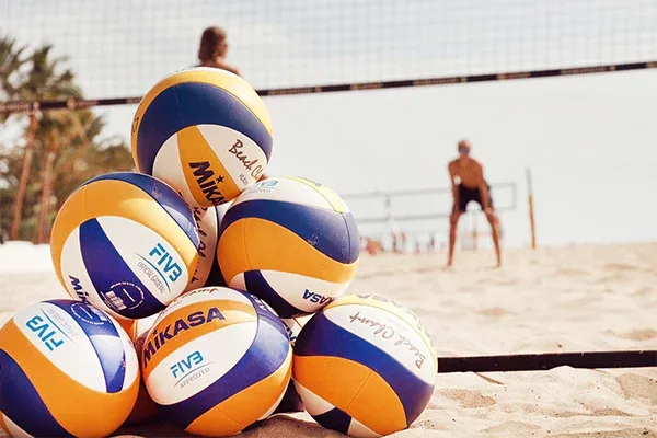 Flera volleyboll bollar som ligger på stranden med människor som spelar volleyboll i bakgrunden