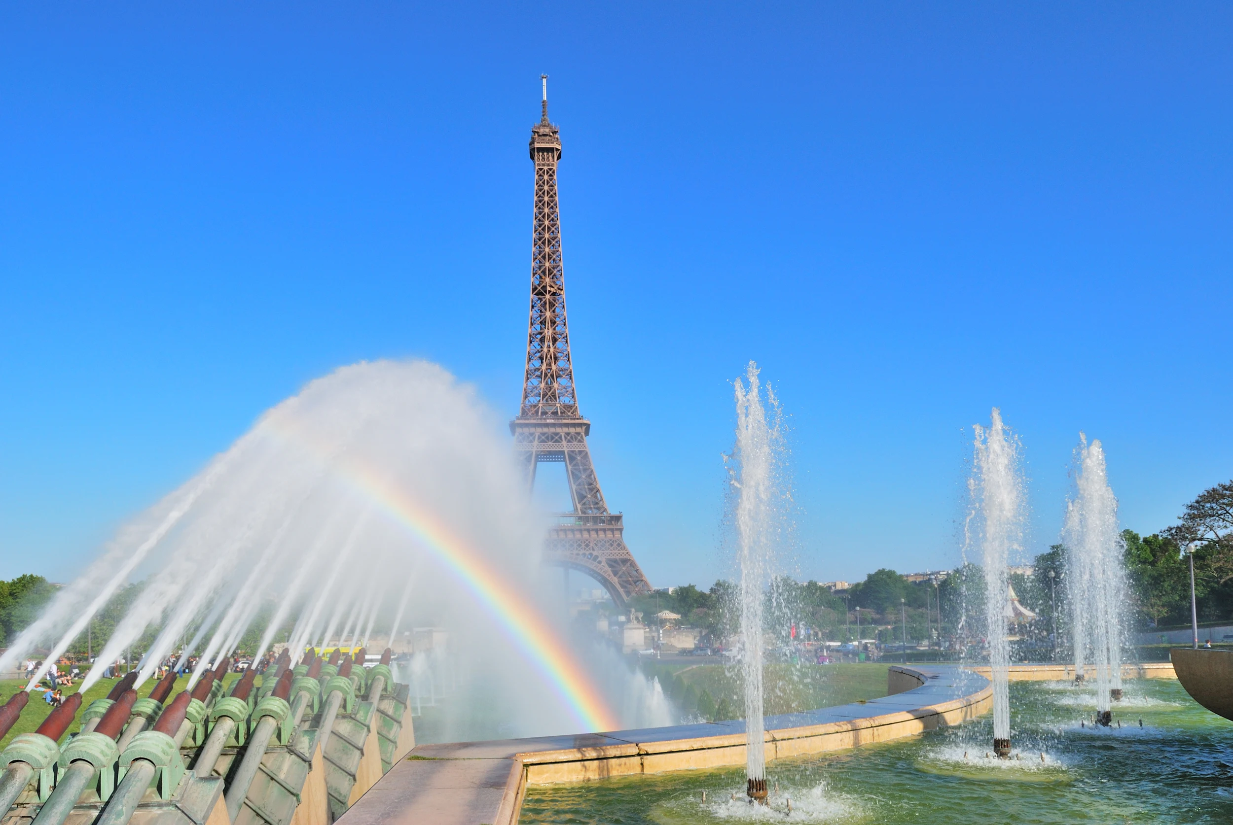 Fontäner som skapar en regnbåge framför Eiffeltornet i Paris