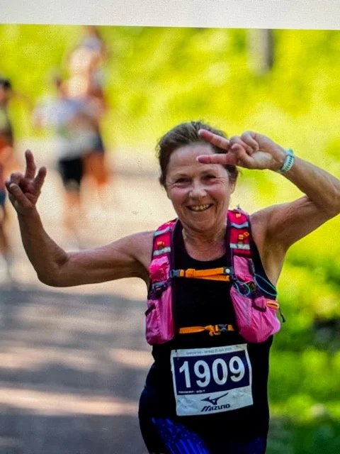 Profilbilde av Monica Hoel der hun løper ute i sort treningssinglet og bukse med rosa drikkesekk og holder armene opp i været.