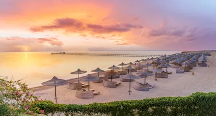 Strand i Hurghada med parasoller och solsängar vid lugnt hav i solnedgångsljus.