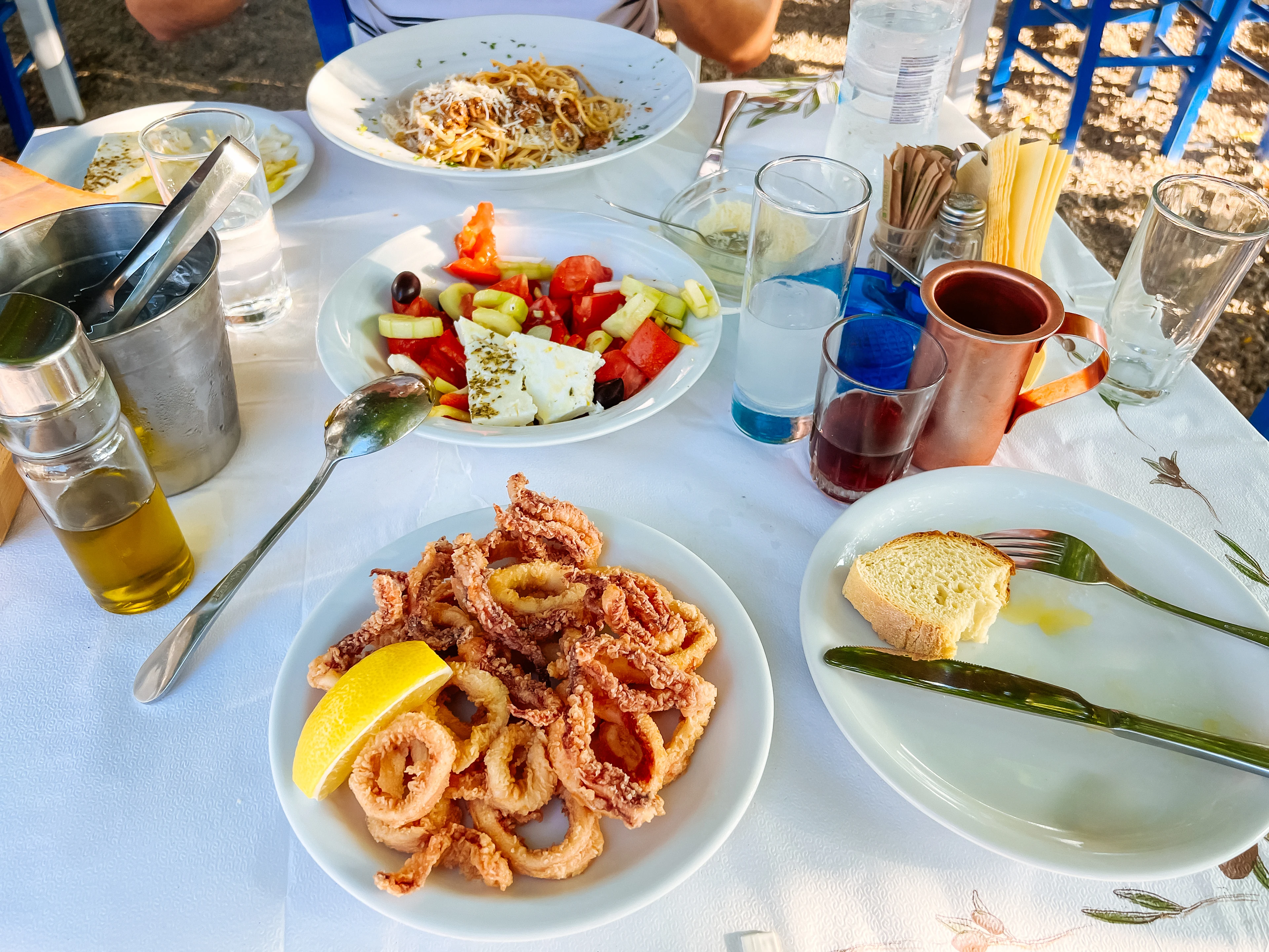 Et bord dækket med blæksprutte, græsk salat og pasta