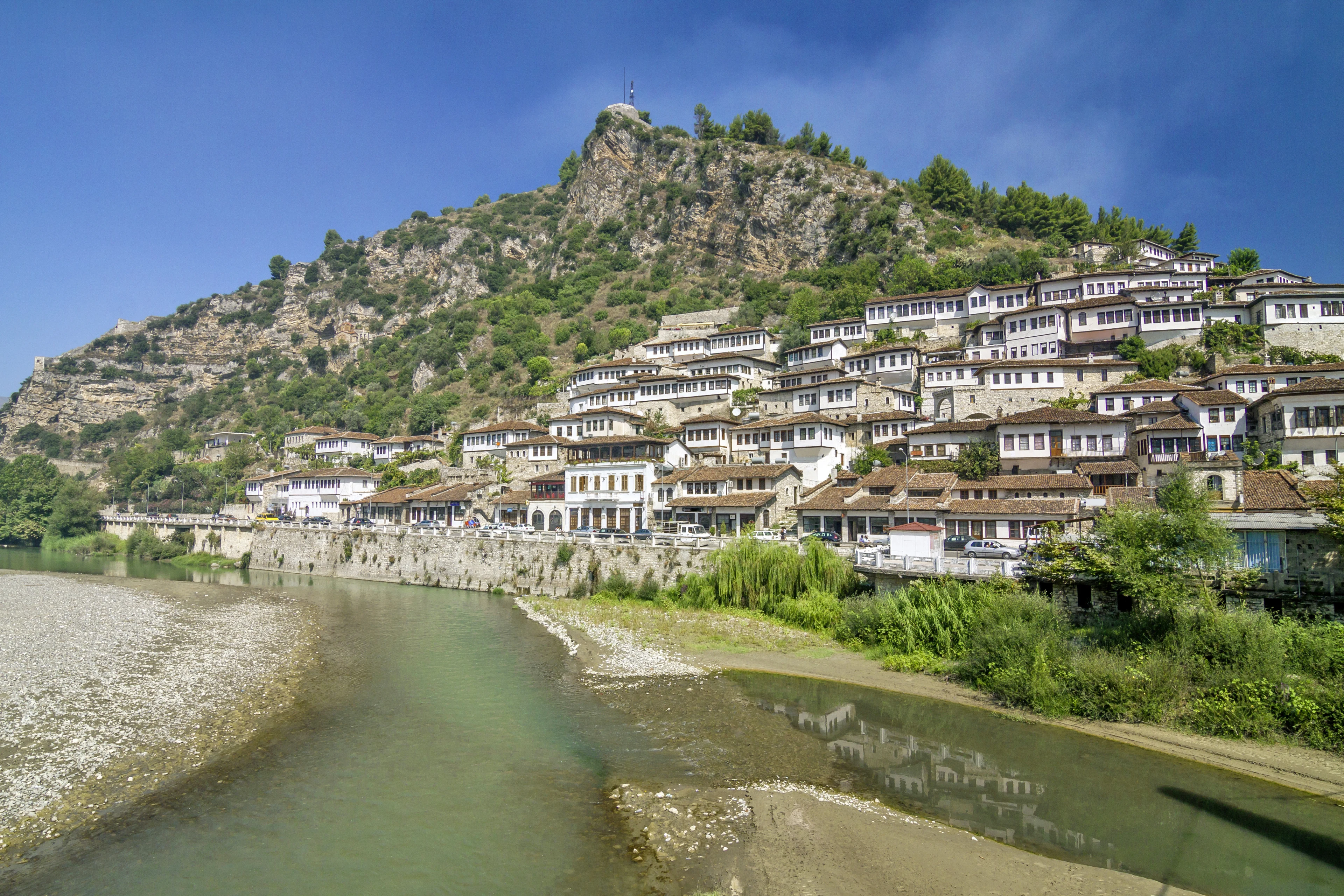 Landsbyen Berat med hvite hus og en elv som renner forbi og fjell i bakgrunnen