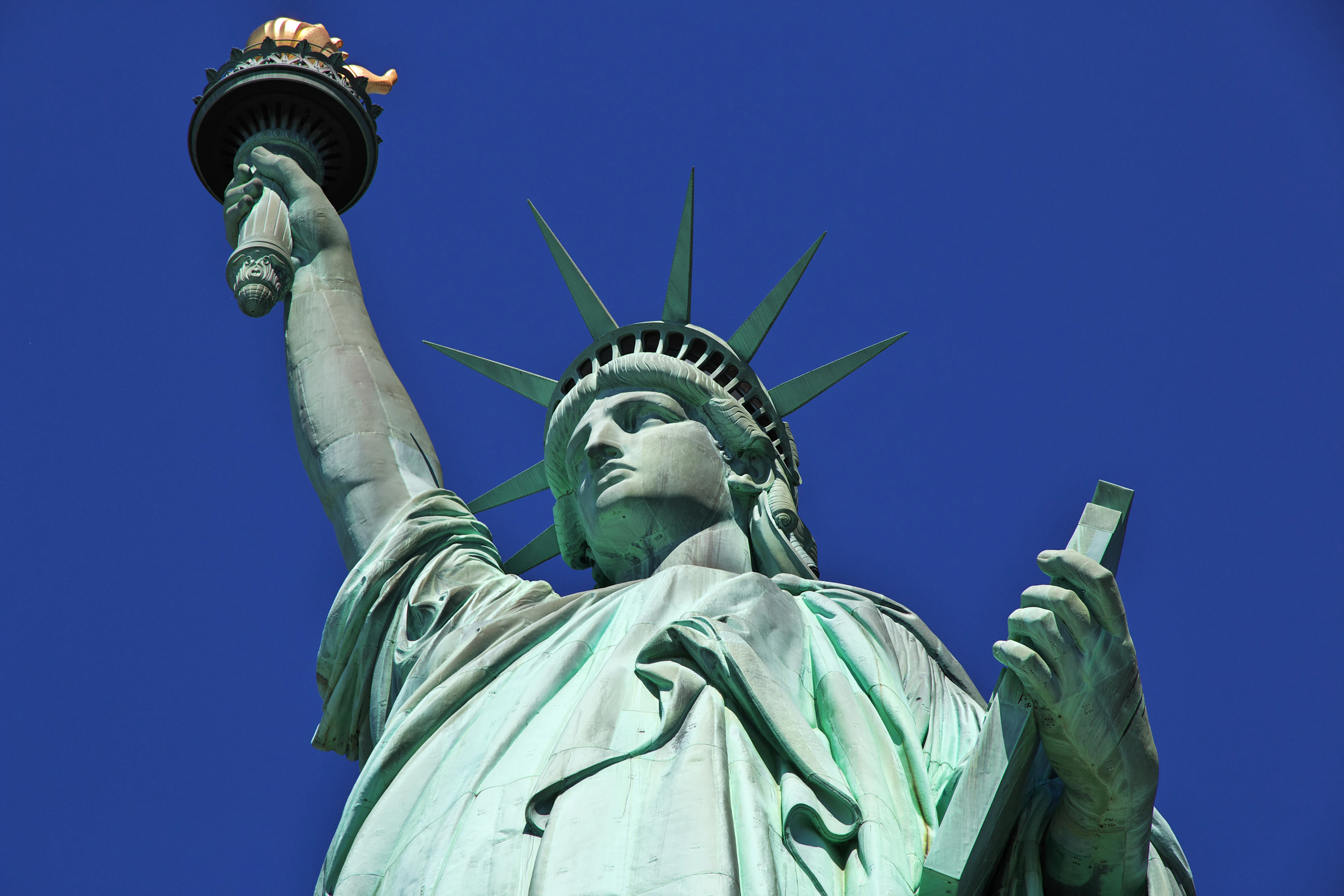 Lähikuva Vapaudenpatsaasta Liberty Islandilla. Kuvassa näkyvät patsaan kruunu ja soihtu kirkkaan sinistä taivasta vasten.
