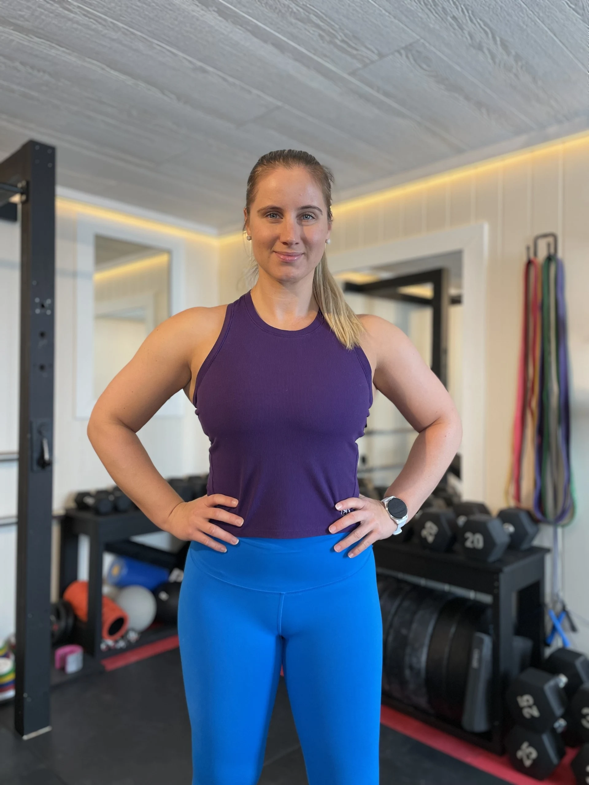 Profilbilde av Stine der hun står i et treningsrom med knallblå treningstights og lilla treningstopp