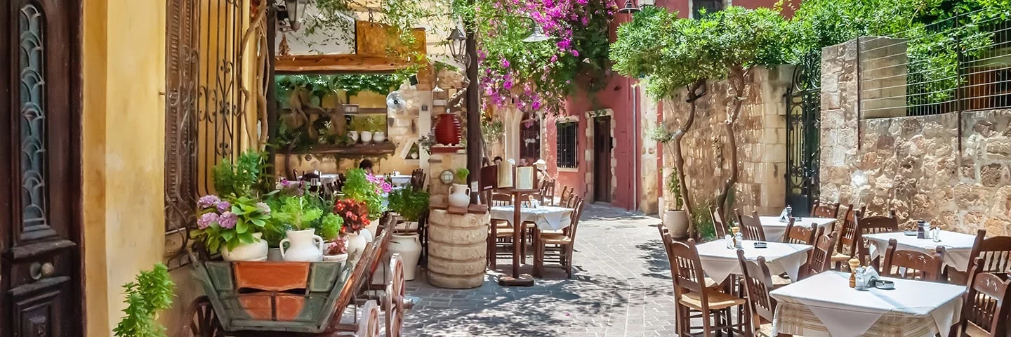 Fra et koselig smug i Chania med bord, stoler og planter