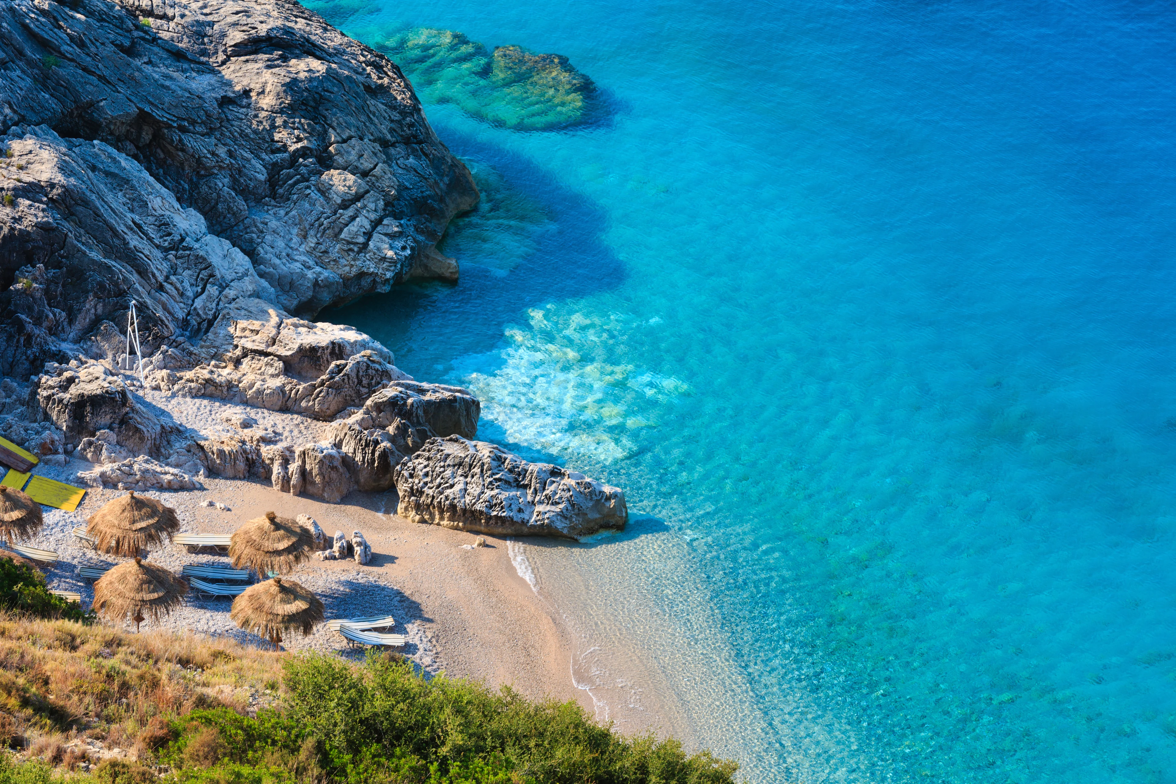 liten gömd strand i albanien med solstolar och parasol