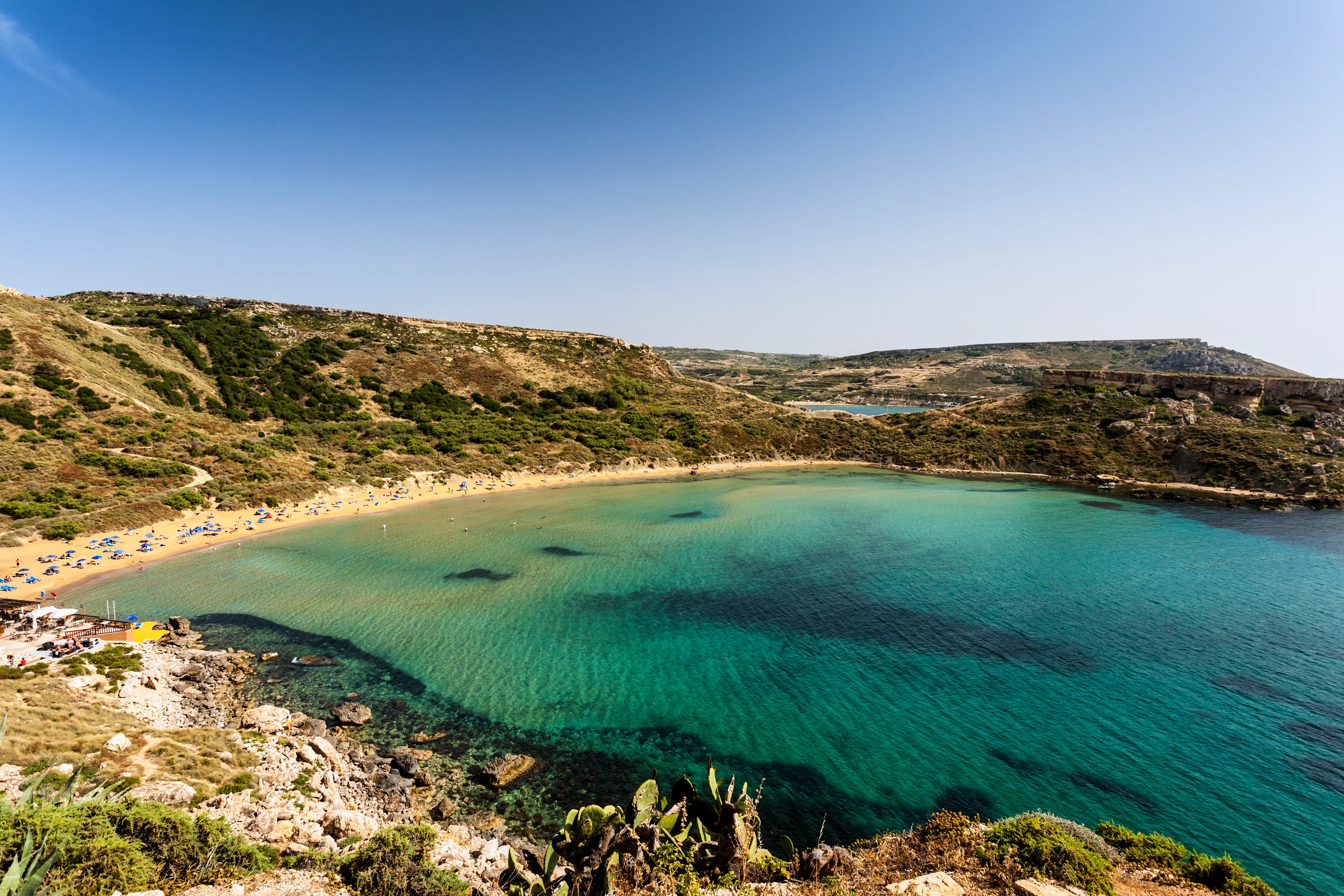 Panoramautsikt över Ghajn Tuffieha Bay på Malta med turkost hav, gyllene sandstrand och dramatiska klippor som omger viken.