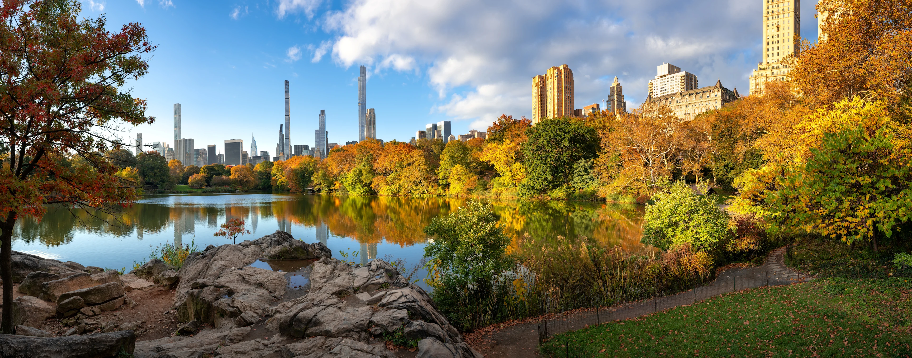 Central Park på Manhattan i New York med efterårsfarver, sø og byens skyline i baggrunden.