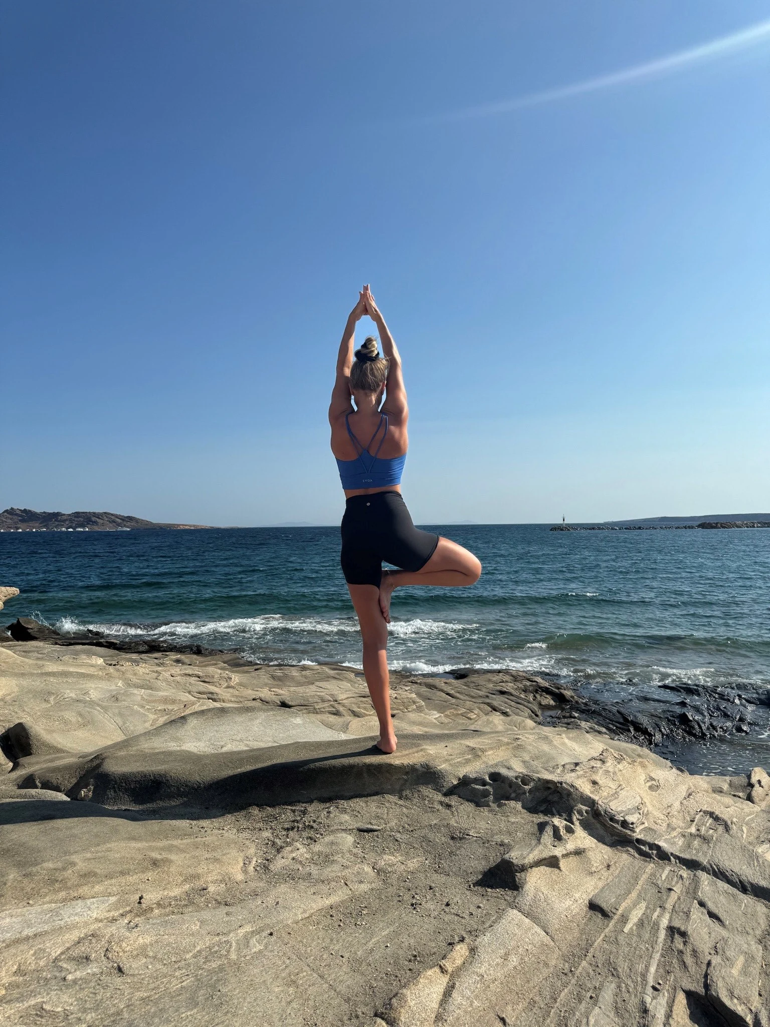 Astrid Salthaug står i yoga posisjon på et svaberg med havet i bakgrunnen. 