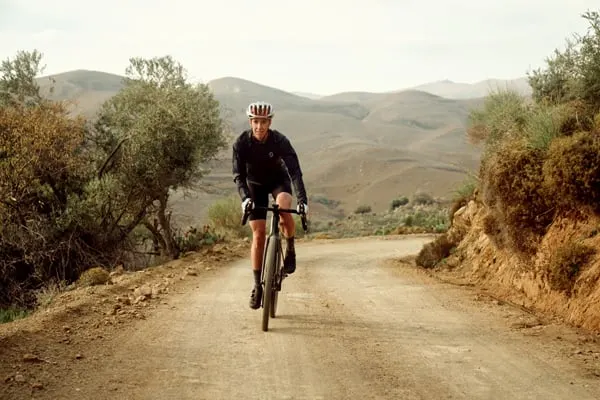 Cyklist på grusväg med berg i bakgrunden 