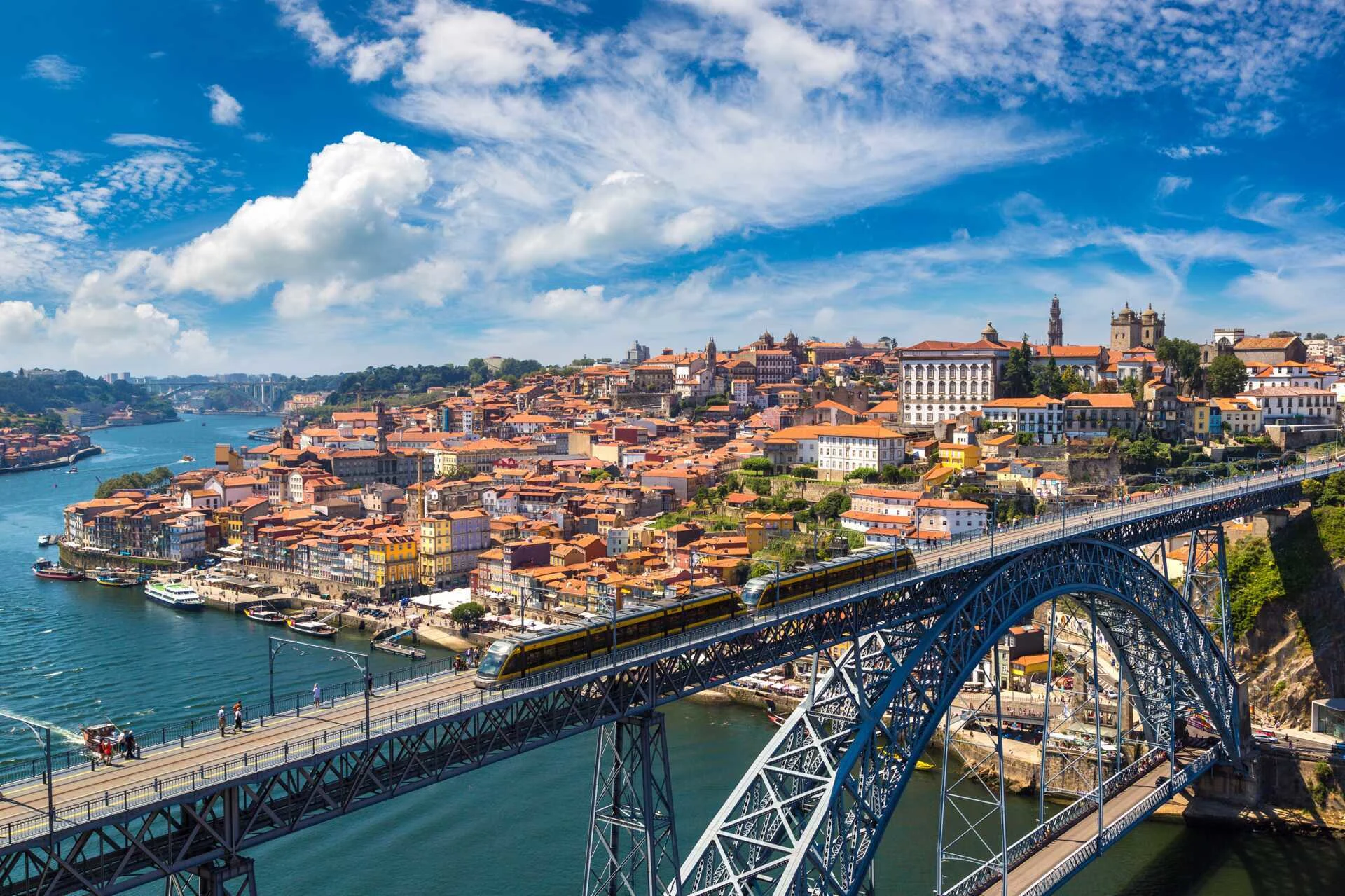 Udsigt over Porto, Portugal med den ikoniske Luís I-bro, der spænder over Douro-floden, og traditionelle portugisiske bygninger langs flodbredden under en klar blå himmel.