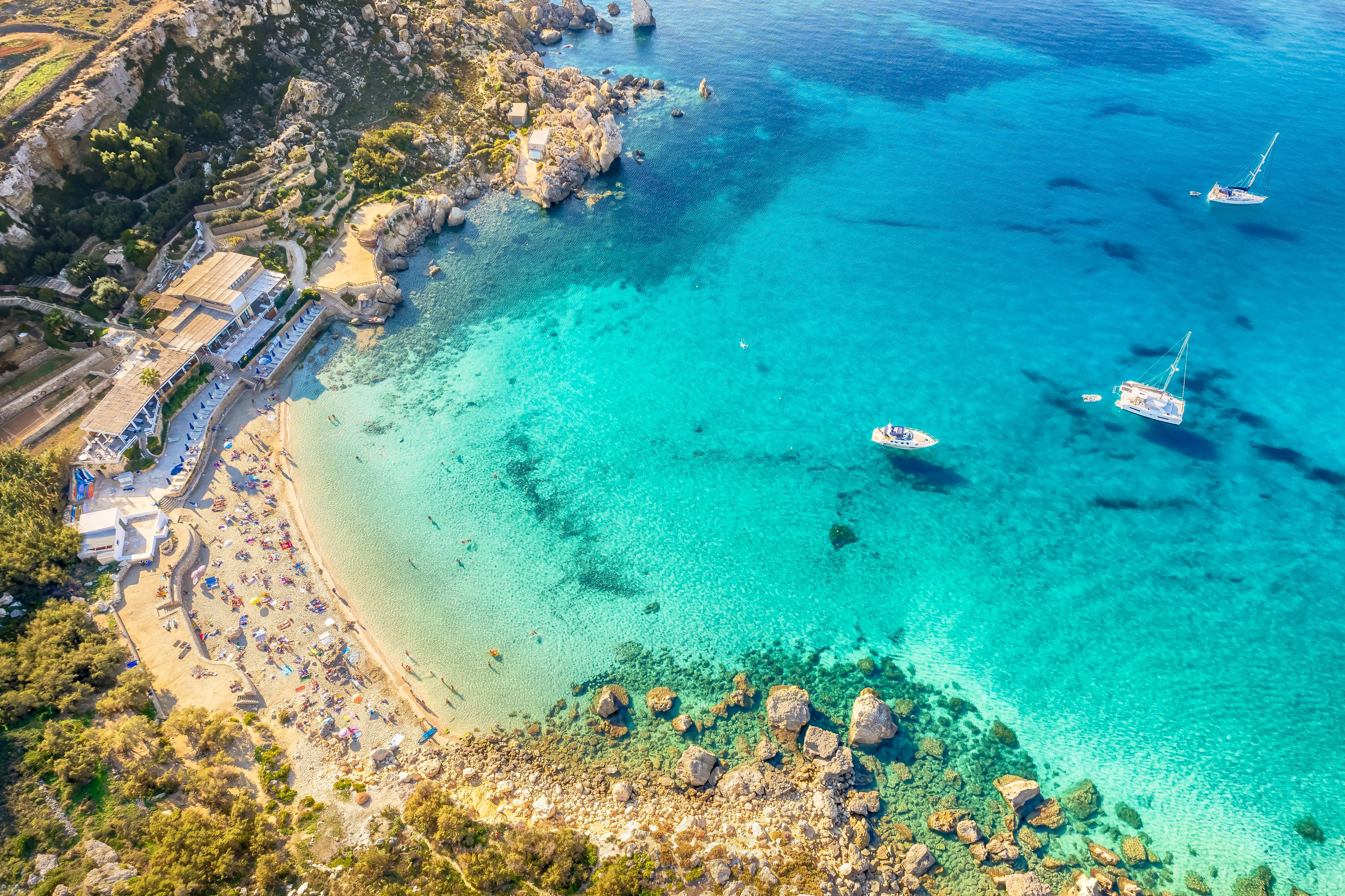 Vacker strand med turkost vatten, segelbåtar och klippkust på Malta.