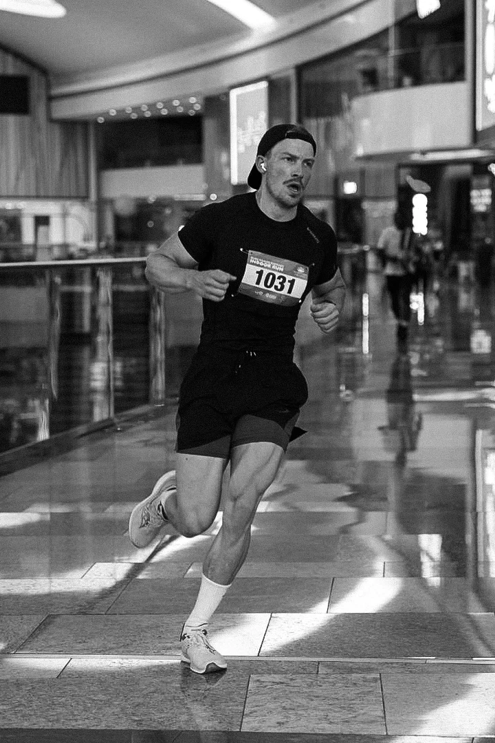 Profilbide av Olav der han løper innendørs ikledd sort treningstøy og caps.