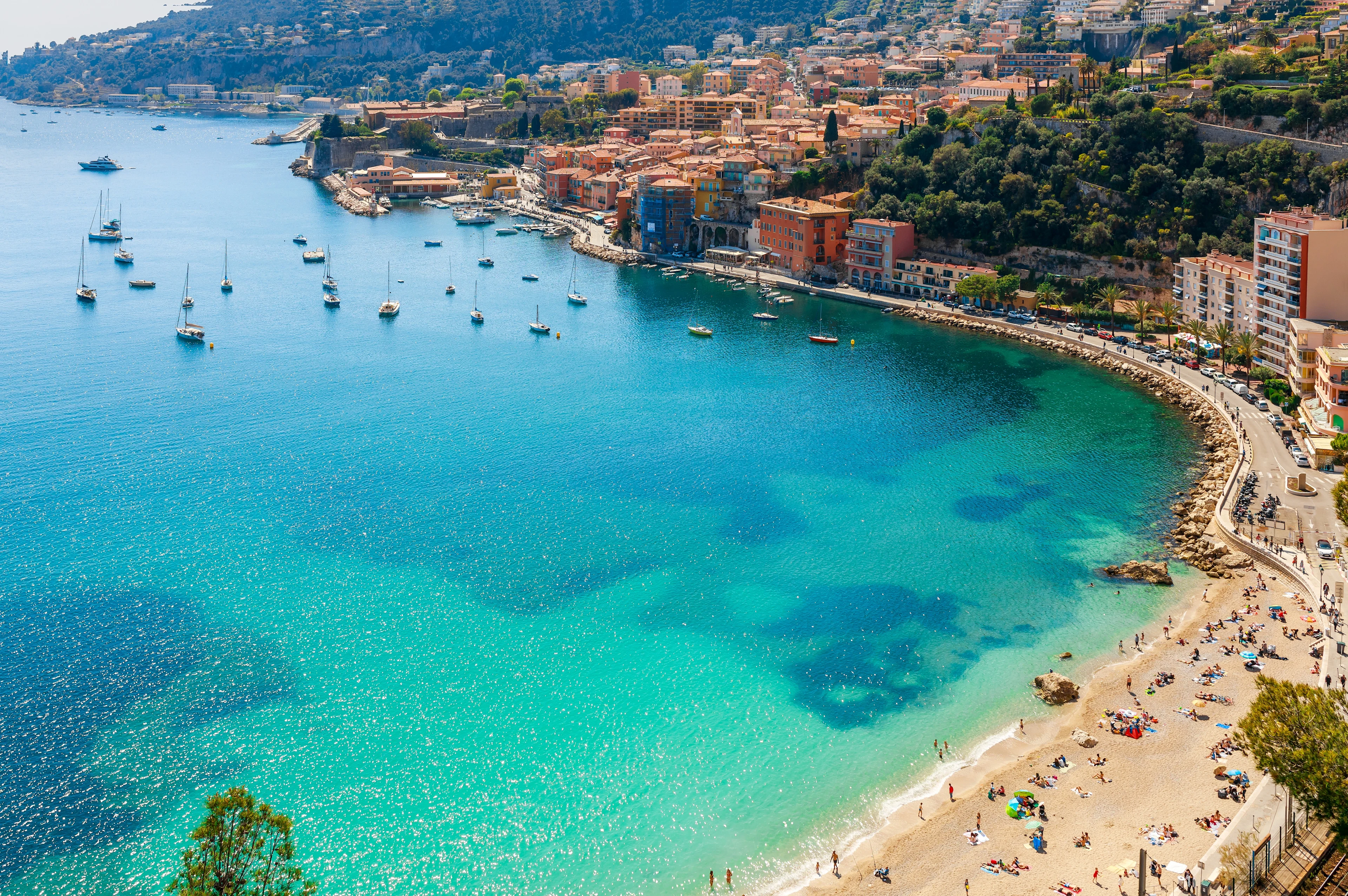 Plage des Marinières i Villefranche-sur-Mer på Franska rivieran med turkost vatten, segelbåtar i bukten och färgglada hus.