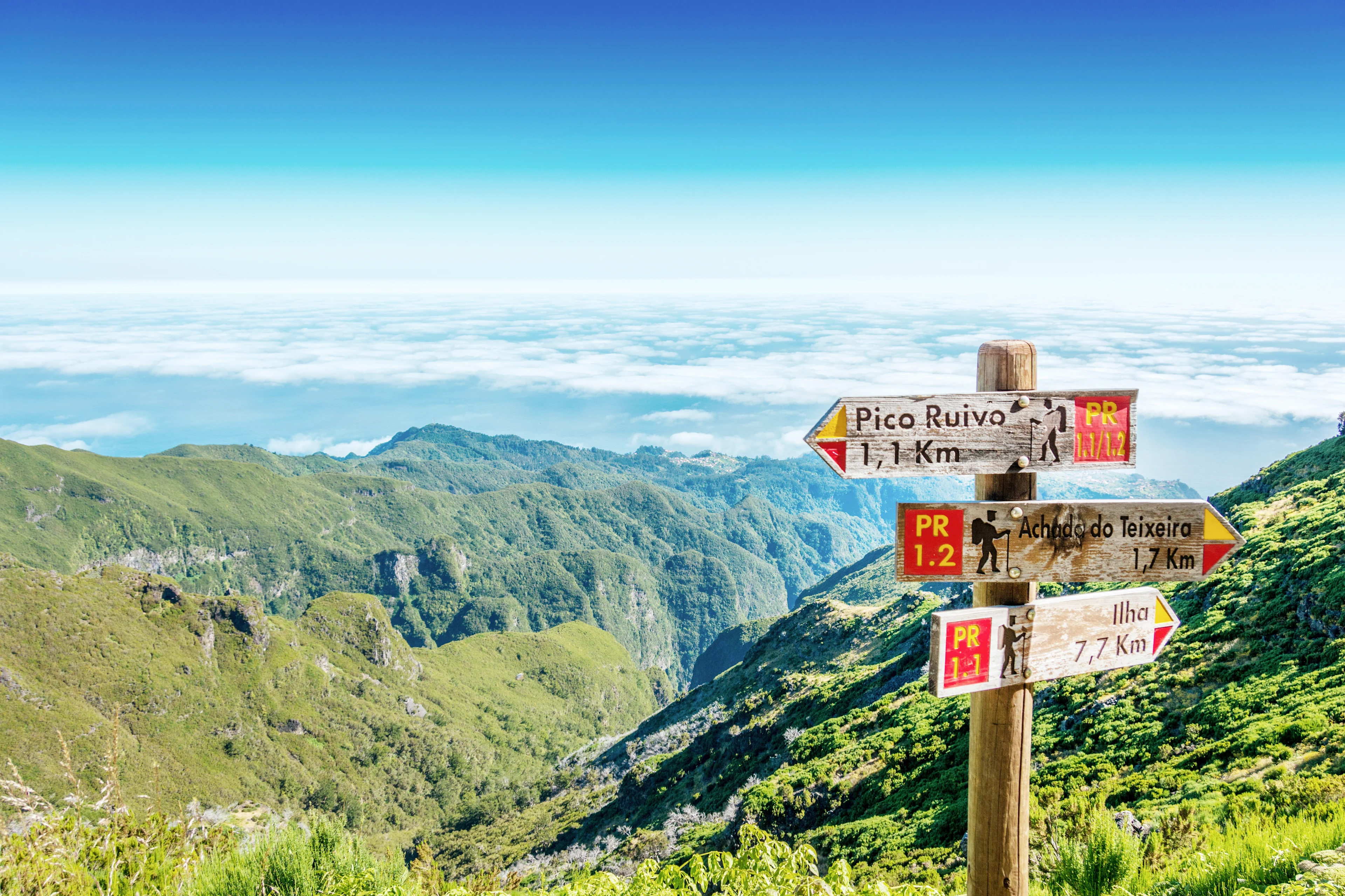 Treskilt som viser turstier høyt oppe i fjellene på Madeira. I bakgrunnen Maderiras magiske natur og havet i horisonten.  