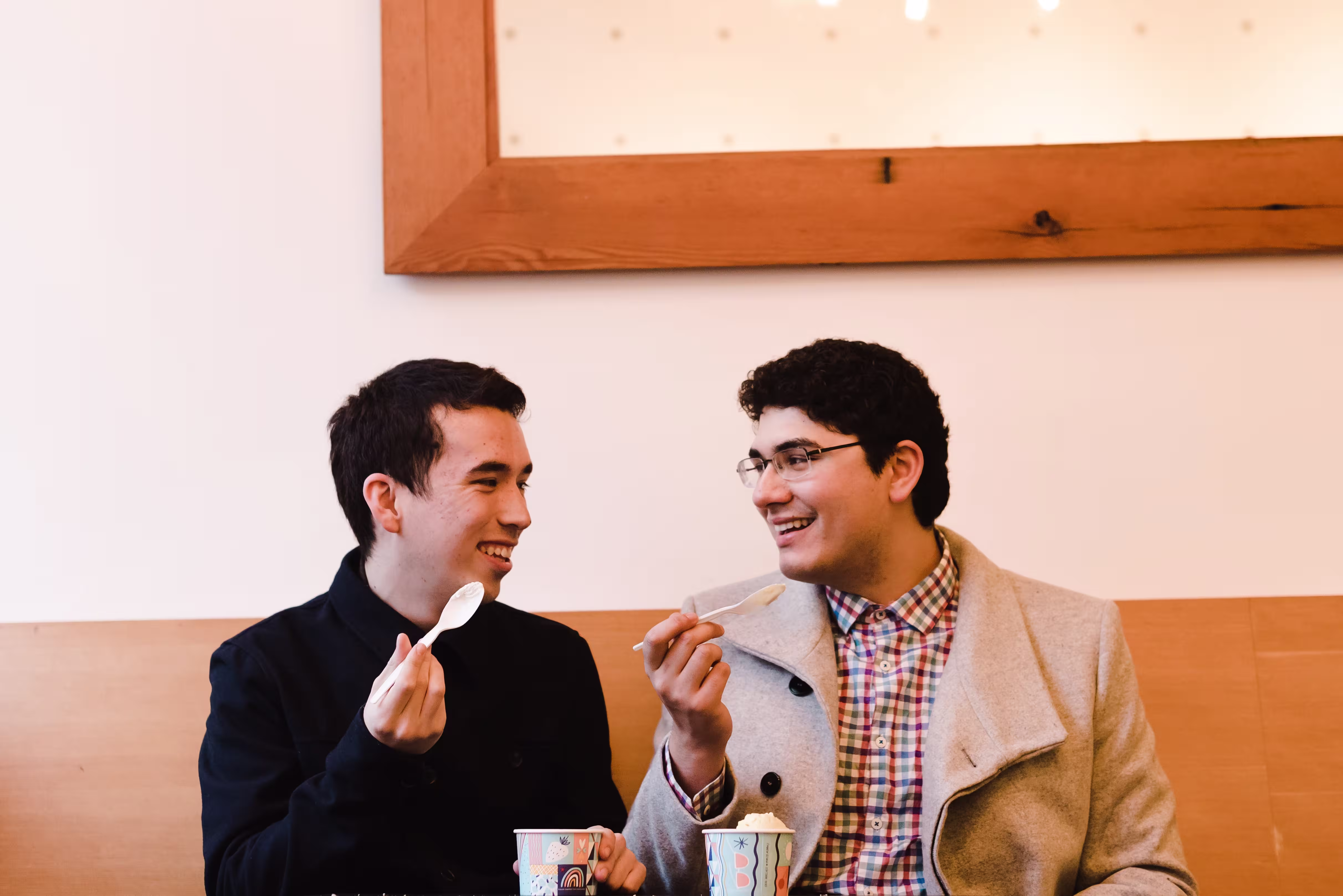 Two people in fall-weather coats enjoy frozen vegan desserts at a restaurant together.
