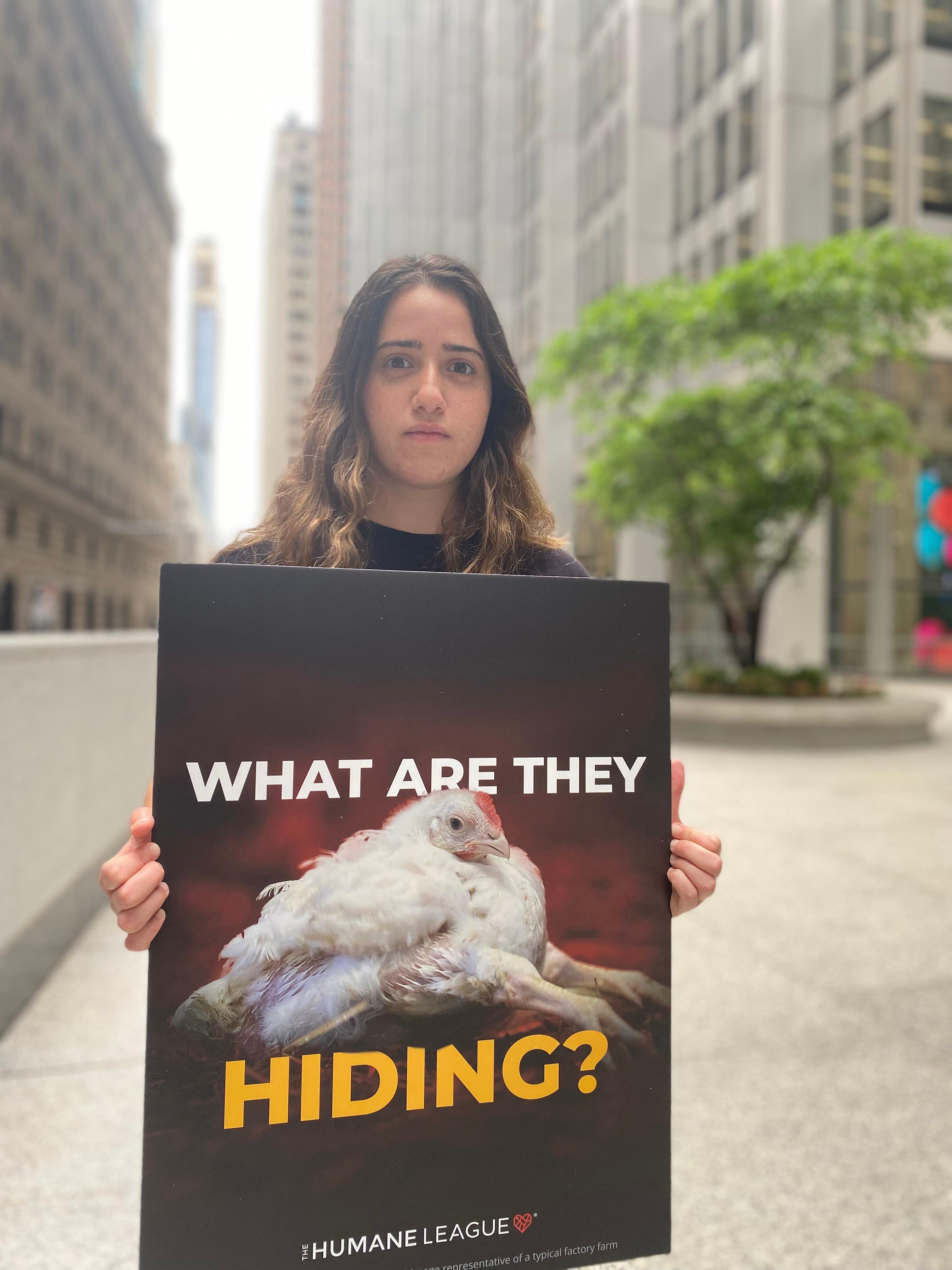 Protester holds a sign with an image of a factory farmed chicken raised for meat that reads: What are they hiding?