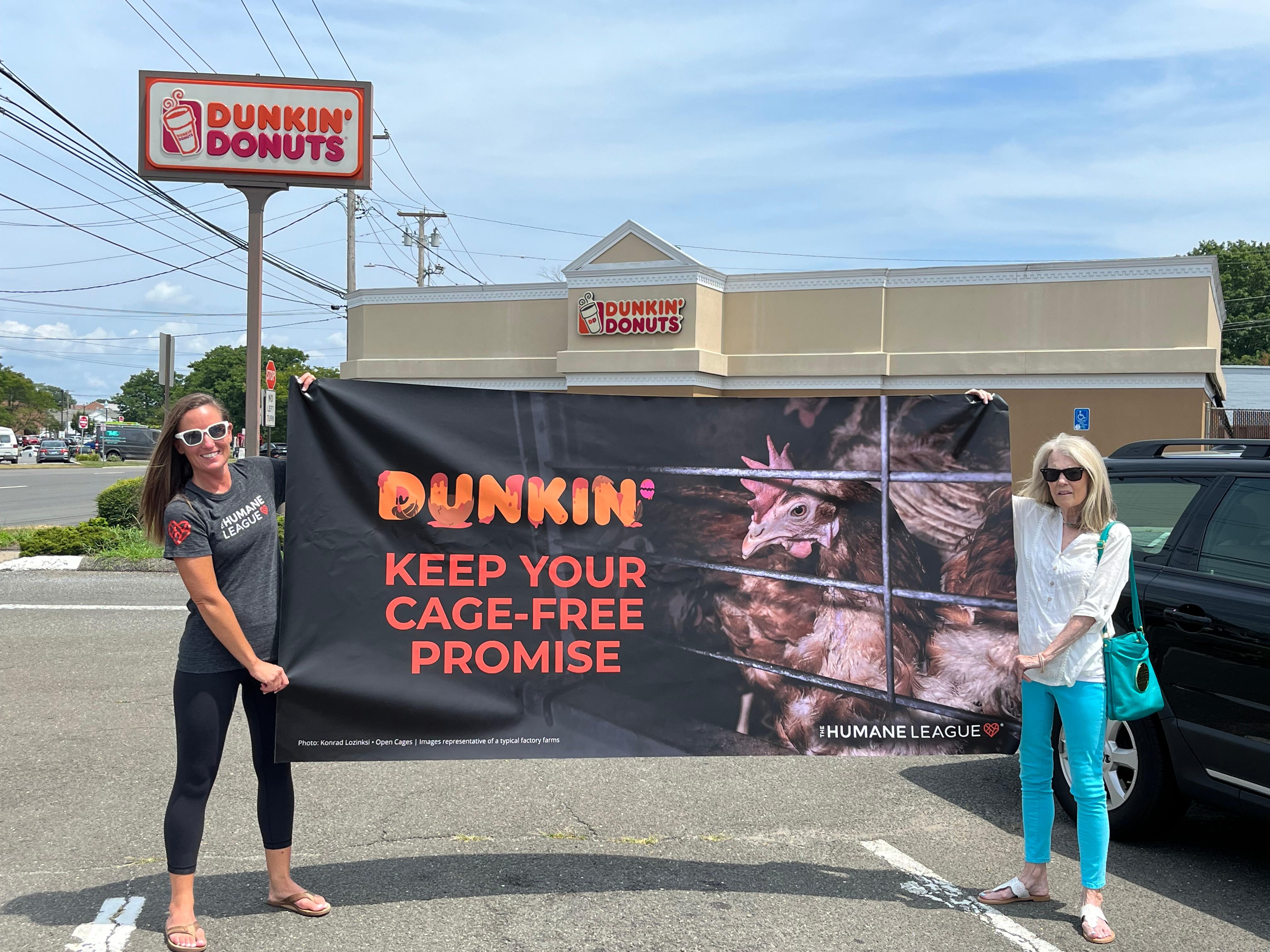 Two women holding banner which reads: "Dunkin' keep your cage-free promise" outside Dunkin' 