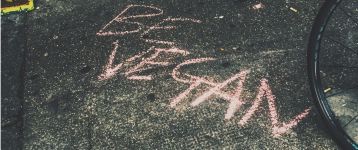 The text "Be Vegan" written on the pavement in chalk