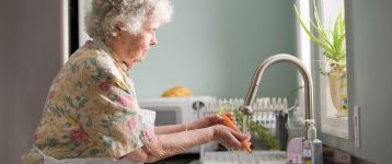 Senior woman washing carrots at the sink