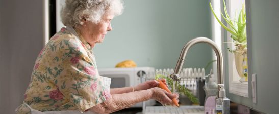Senior woman washing carrots at the sink