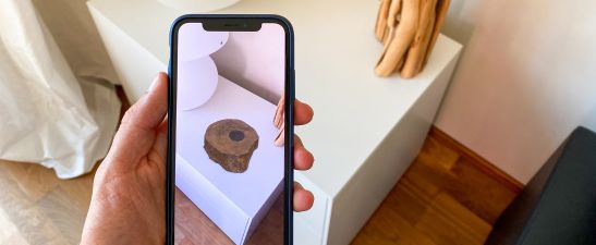 Smartphone shows an augmented reality image of a wooden object on top of a white surface