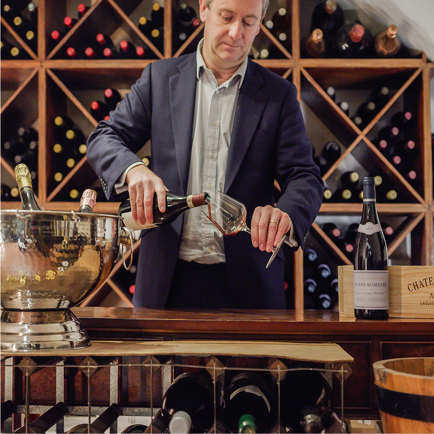 Giles pouring a red wine on a glass in a cellar