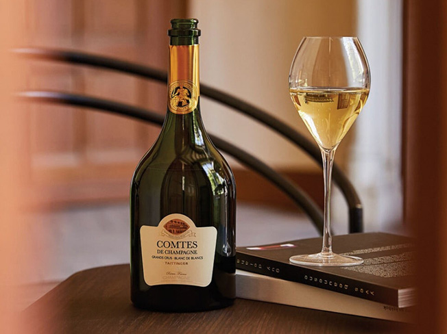 A bottle of Comtes De Champagne on a table with a glass of Champagne on top of two books