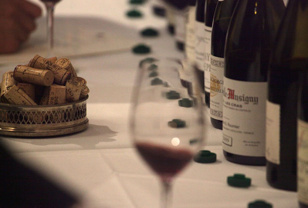 close up of a white table with a glass of wine on it and a row of wine bottles behind the wine glass